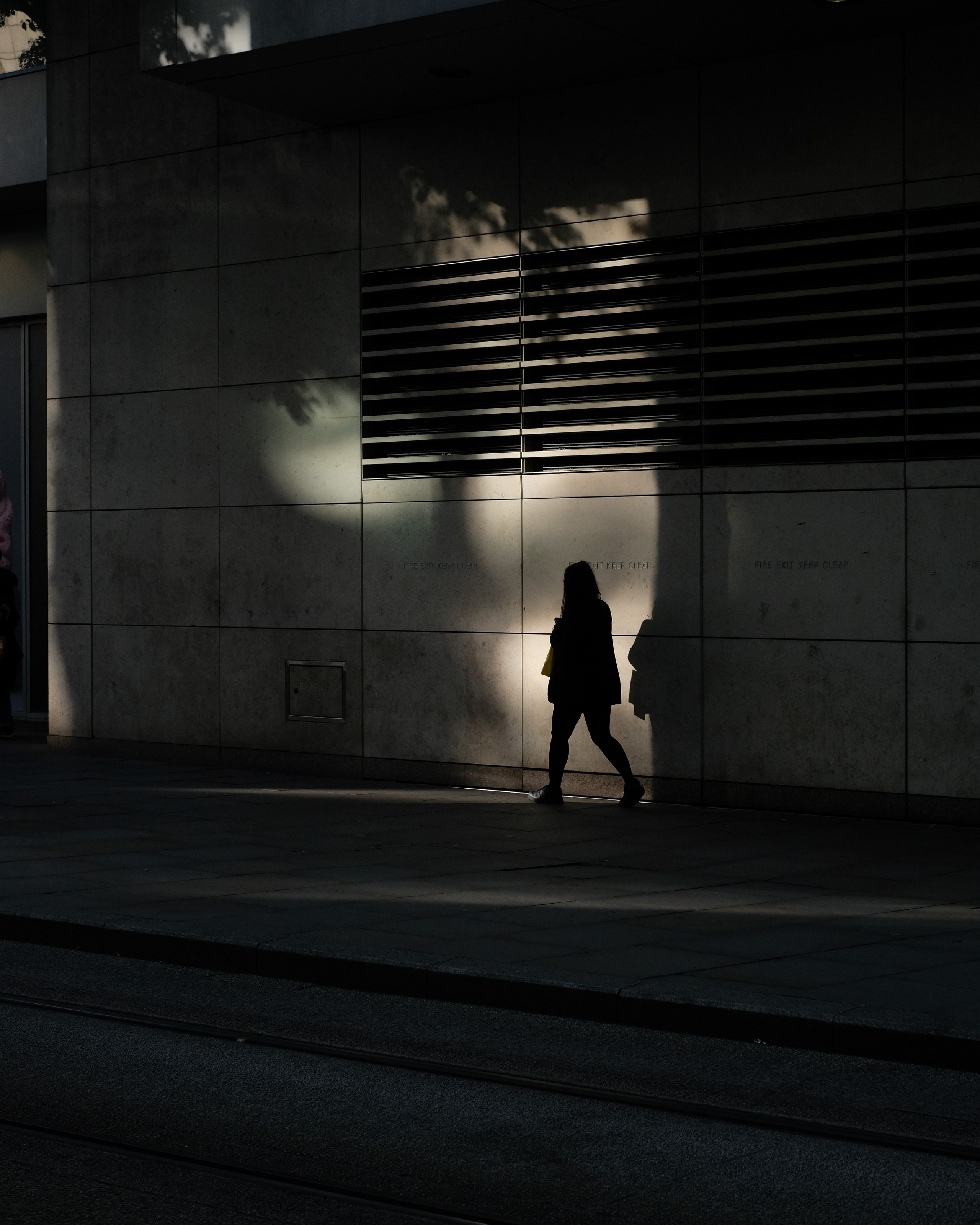 A silhouetted pedestrian crossing a patch of sunlight on a pale wall.