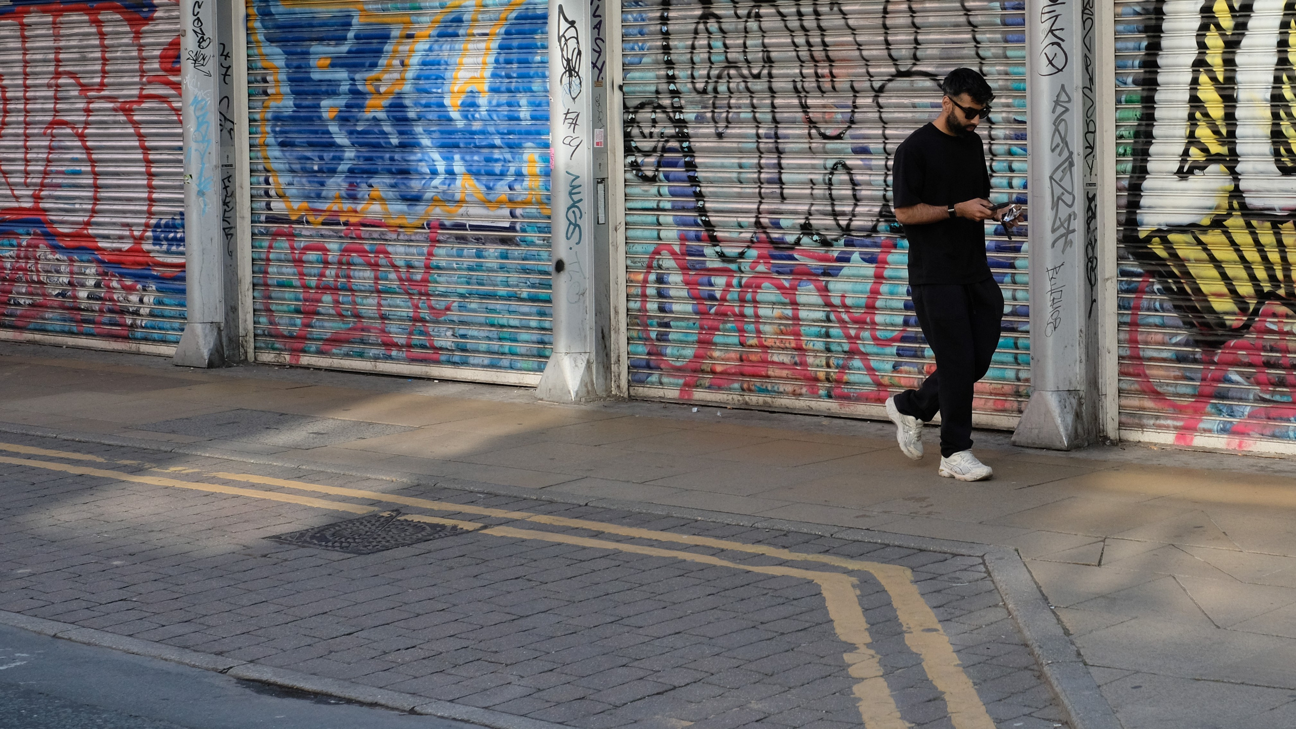A passerby in black walking past colourful graffiti-covered shutters.