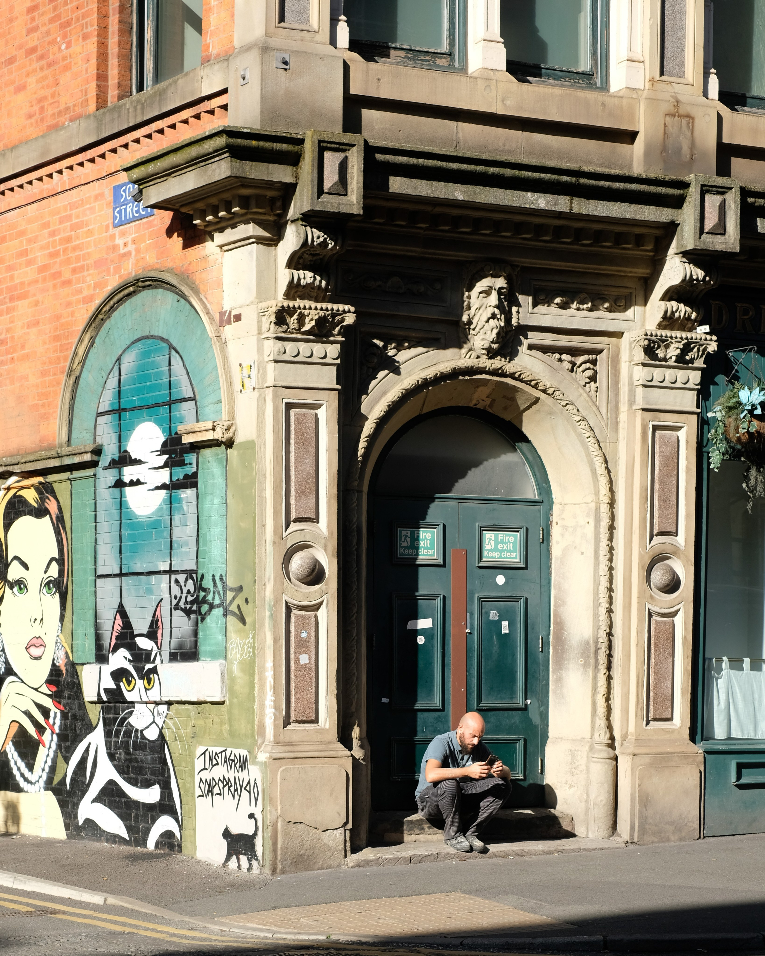 A person seated beneath an ornate green doorway beside painted street art.