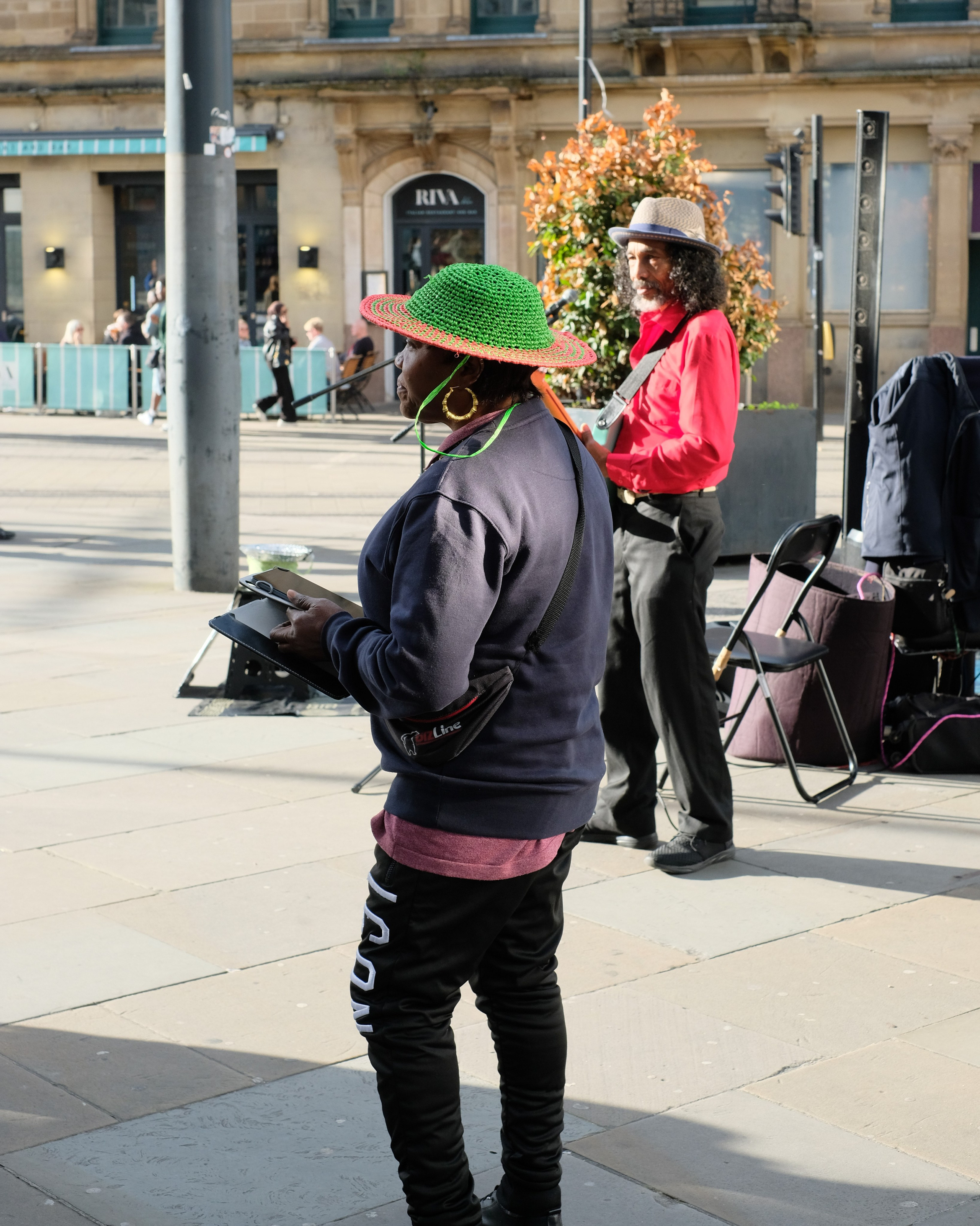 Street musicians in sunlight, with a green hat in the foreground and a red shirt behind.