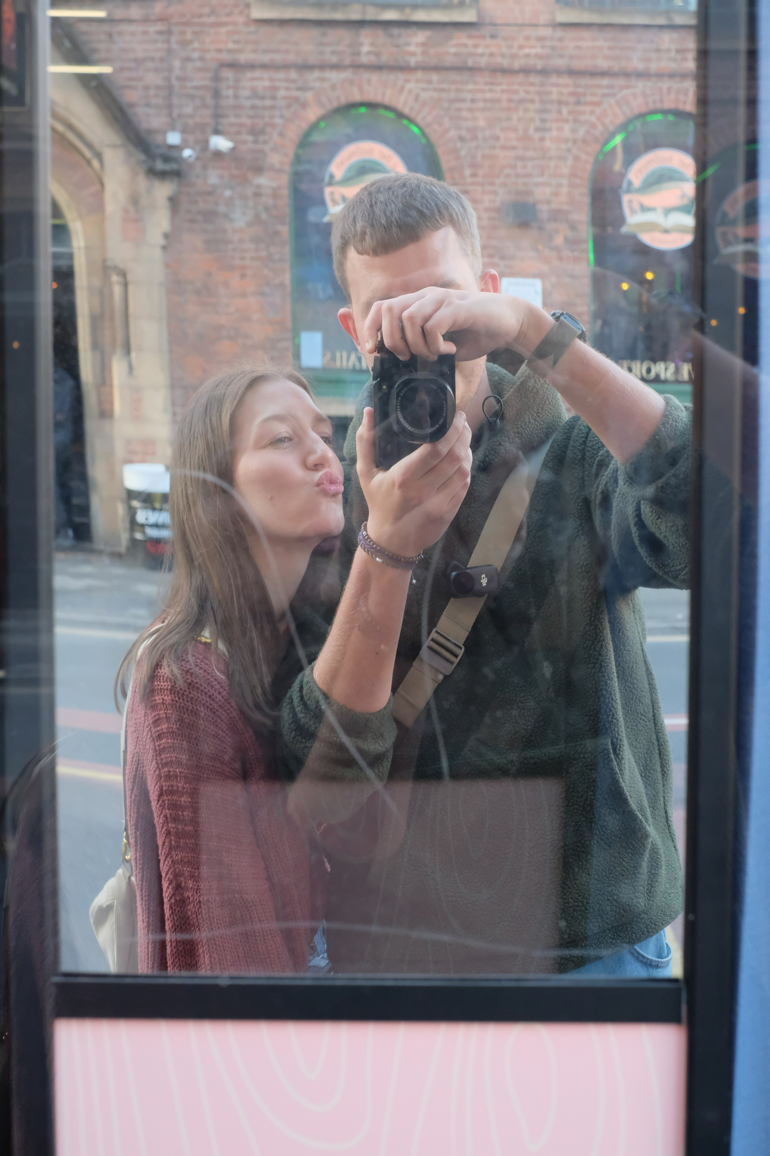 Two people reflected in a Manchester window, one holding a camera.
