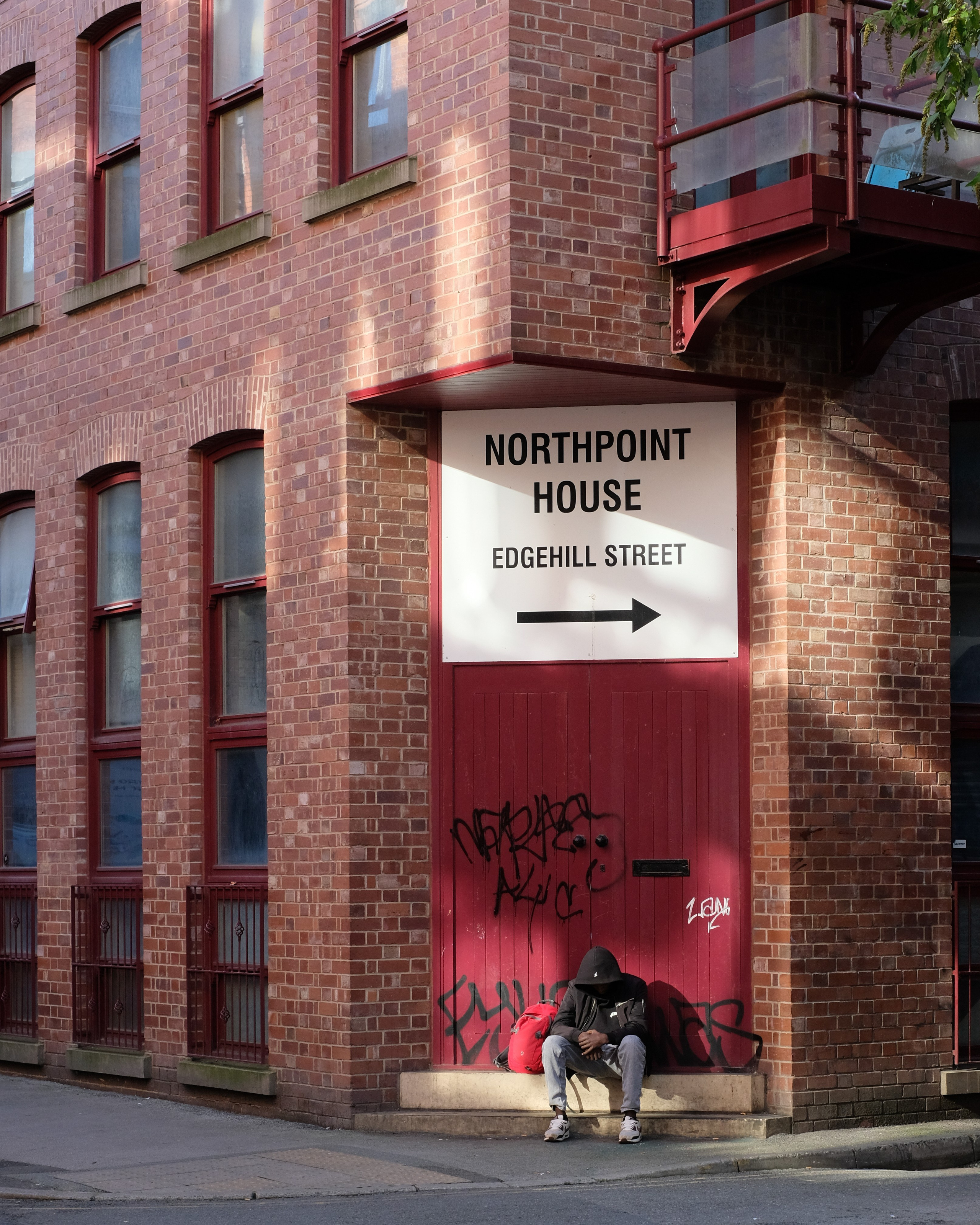 A person seated outside a red doorway at Northpoint House on Edgehill Street.