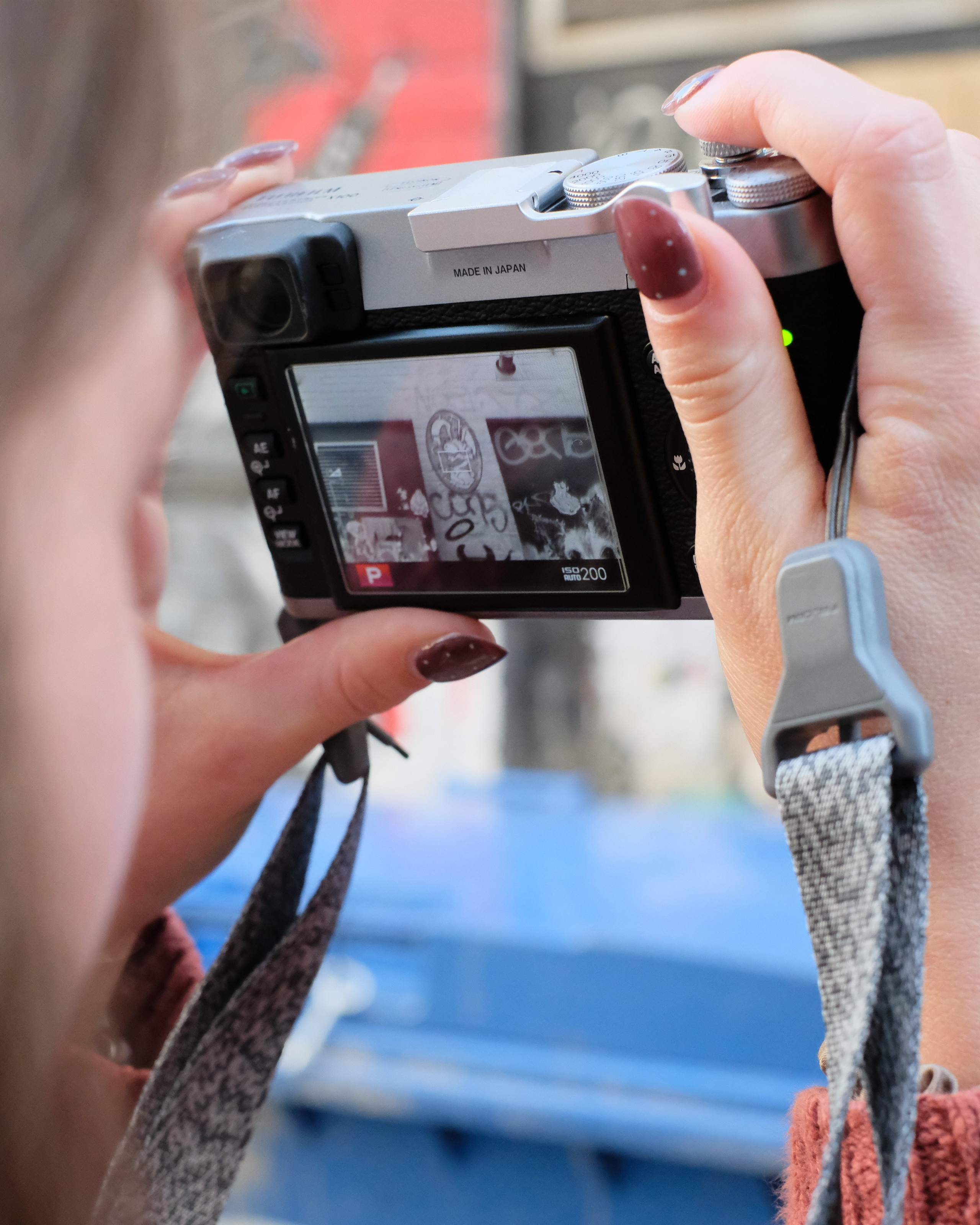 Close-up of hands holding a silver camera while photographing street art.