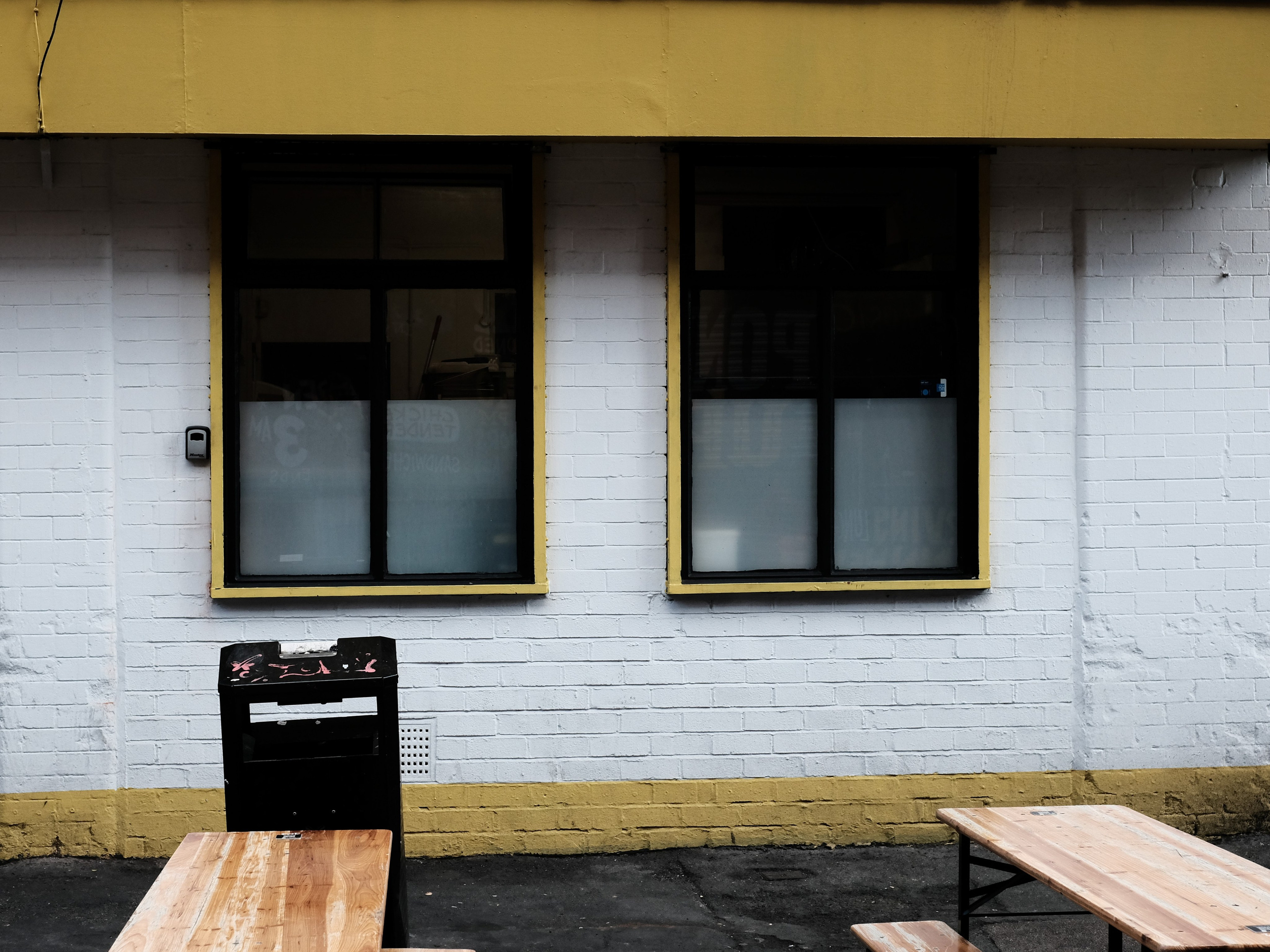 White brick frontage with yellow window frames and wooden outdoor tables in Manchester.