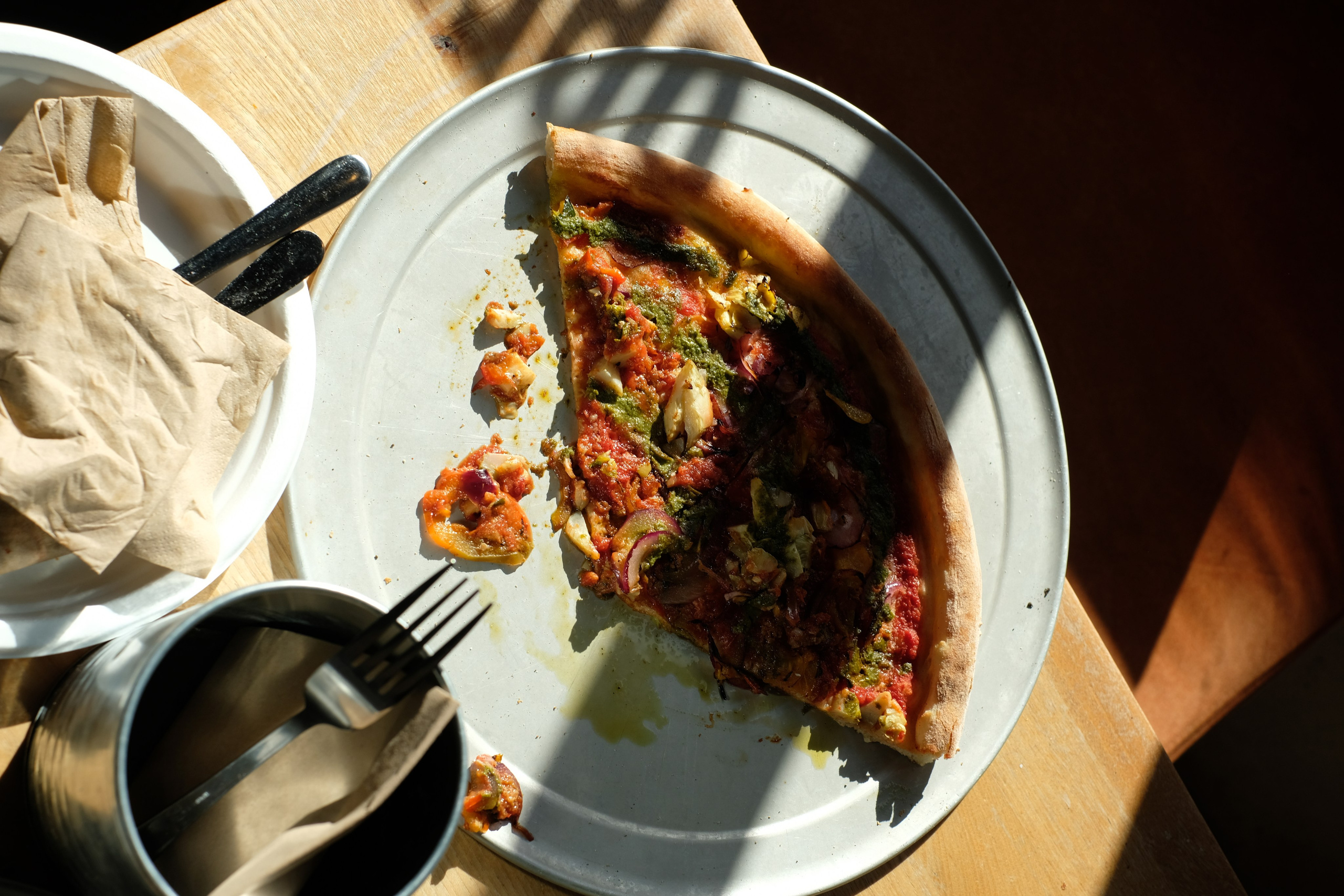 Pizza slice on a white plate with striped window shadows.