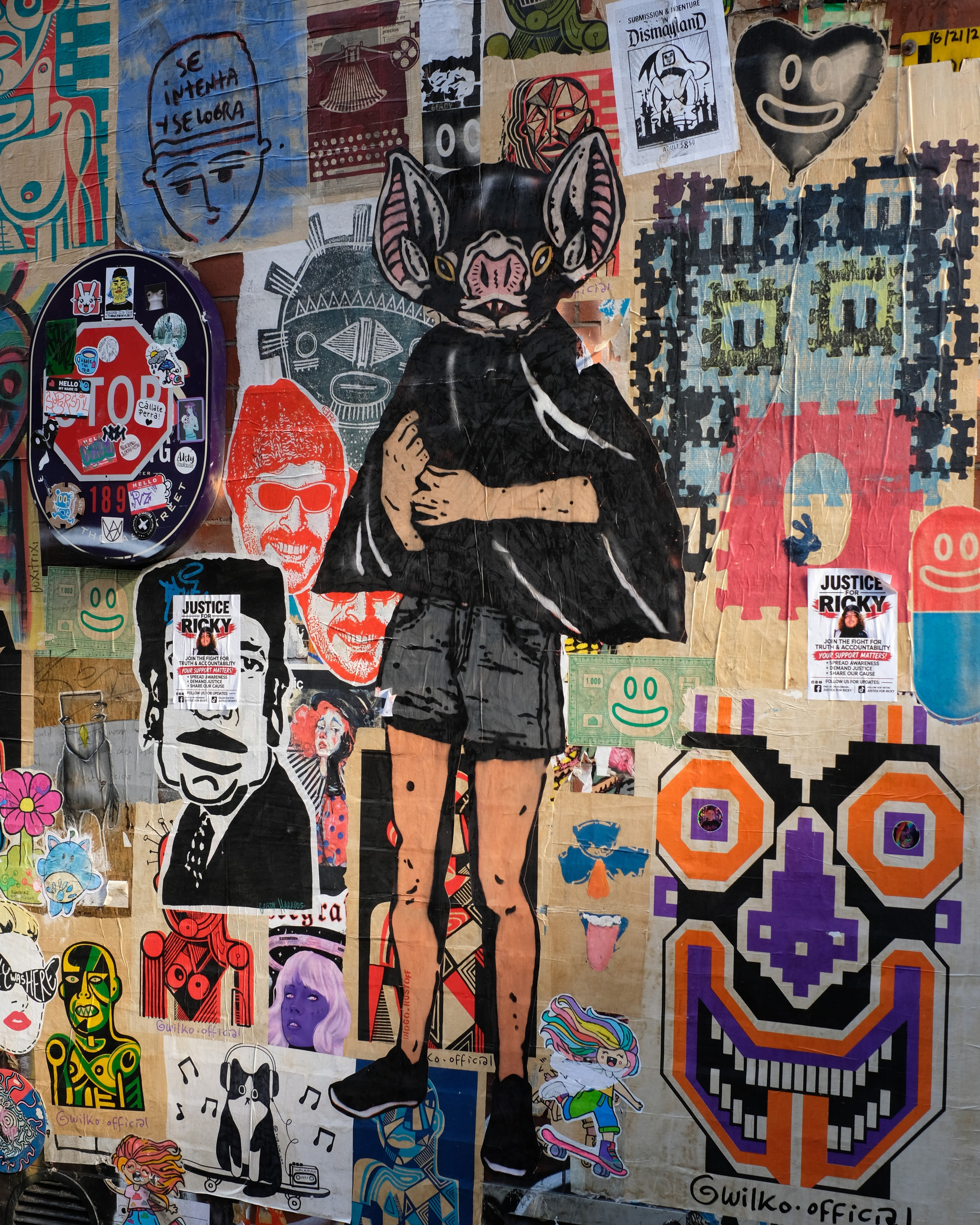 A wall covered in colourful layered paste-up street art in Manchester.
