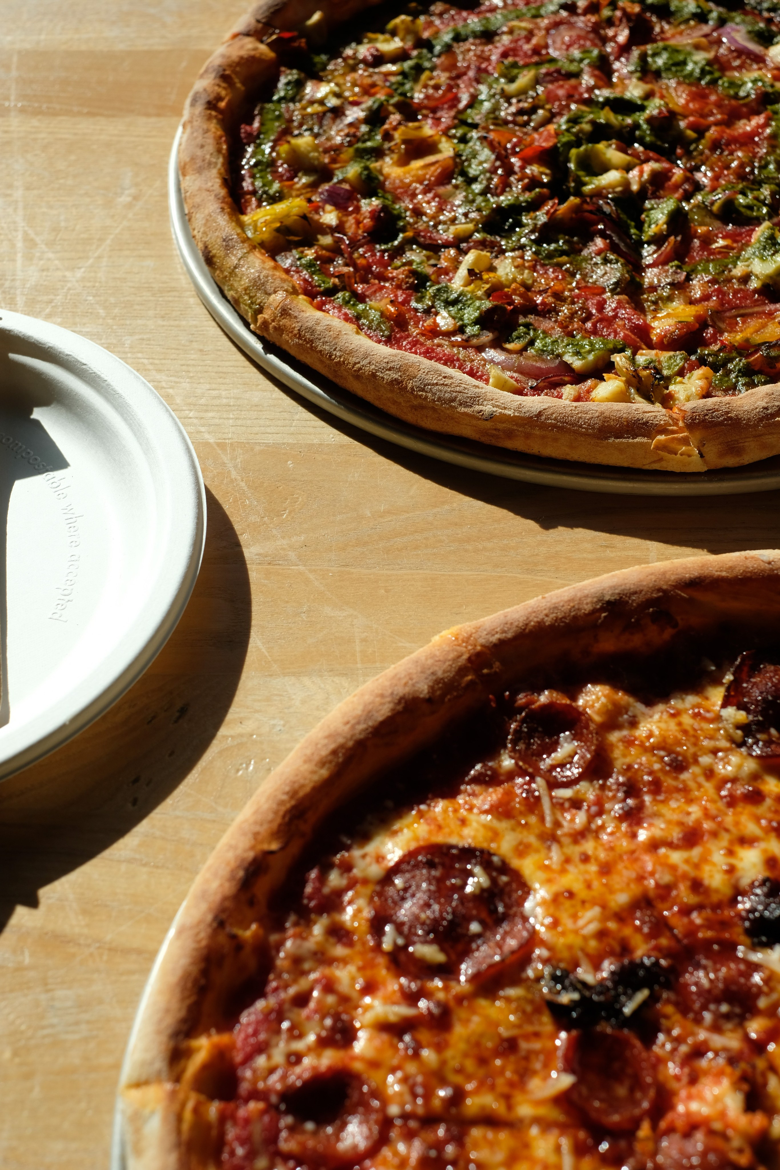 Two pizzas on a wooden table in strong sunlight.