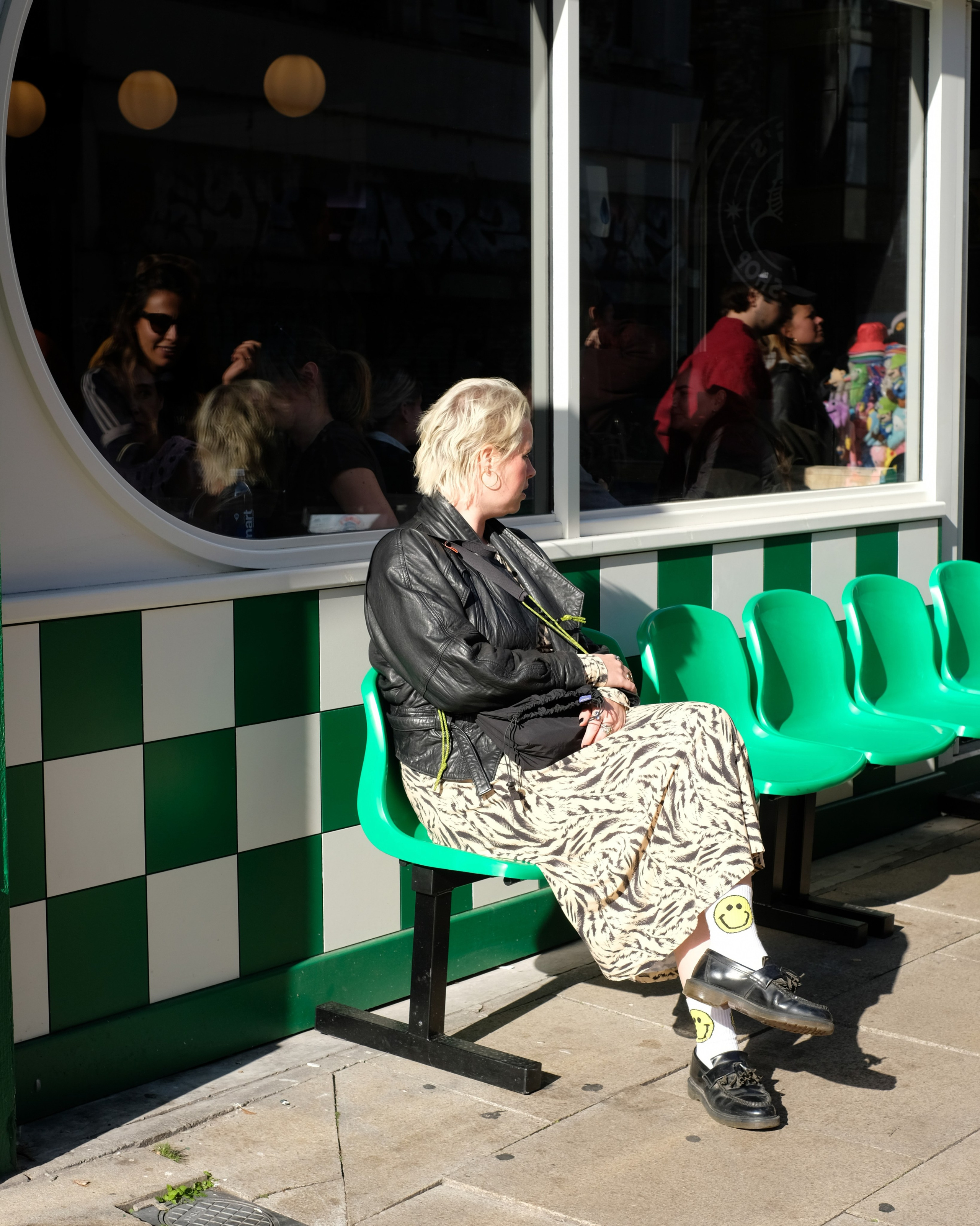 A person in a black leather jacket and smiley-face socks seated on bright green chairs.