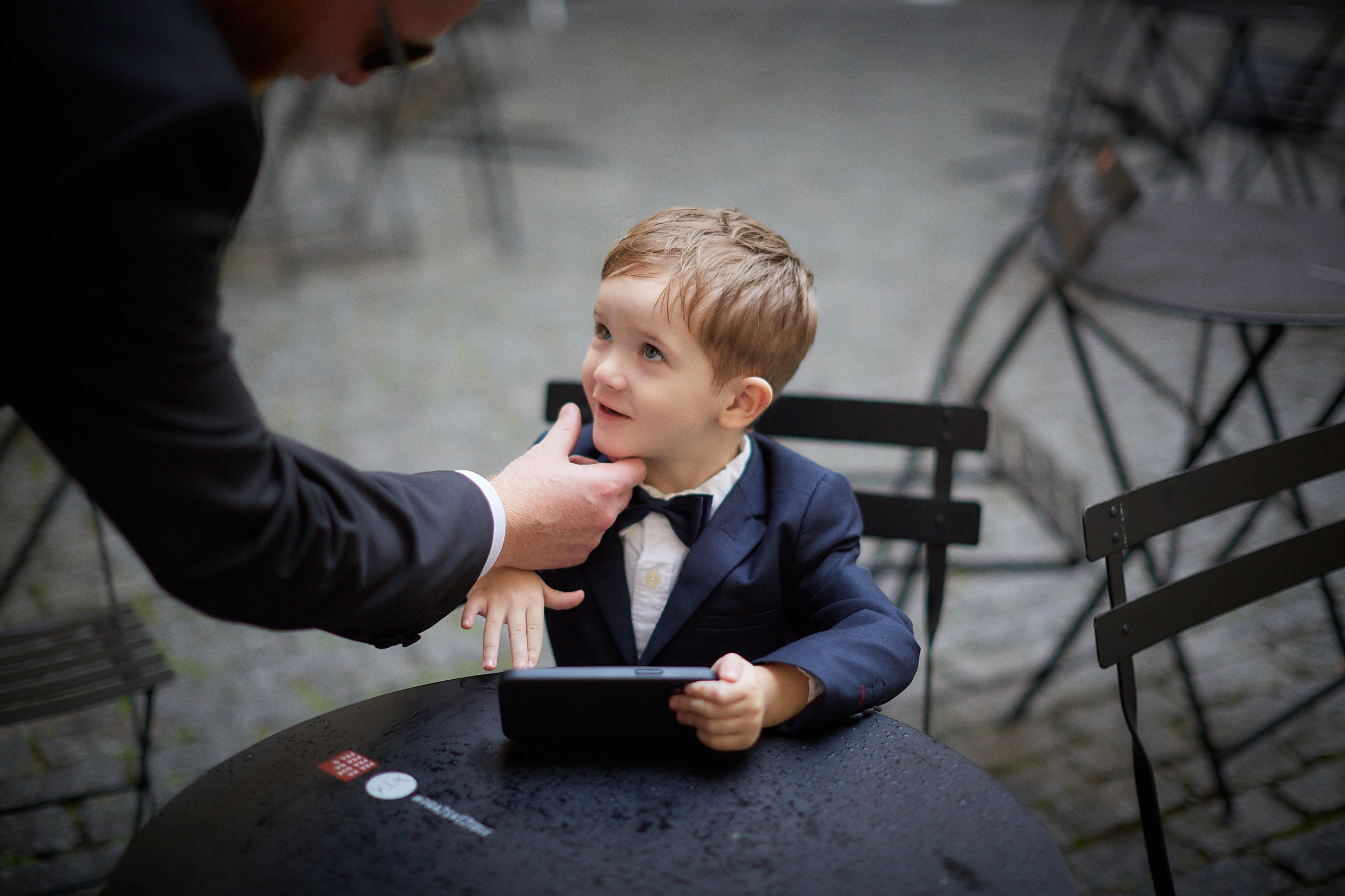 Ring bearer watching screen with father during pre-ceremony wait.