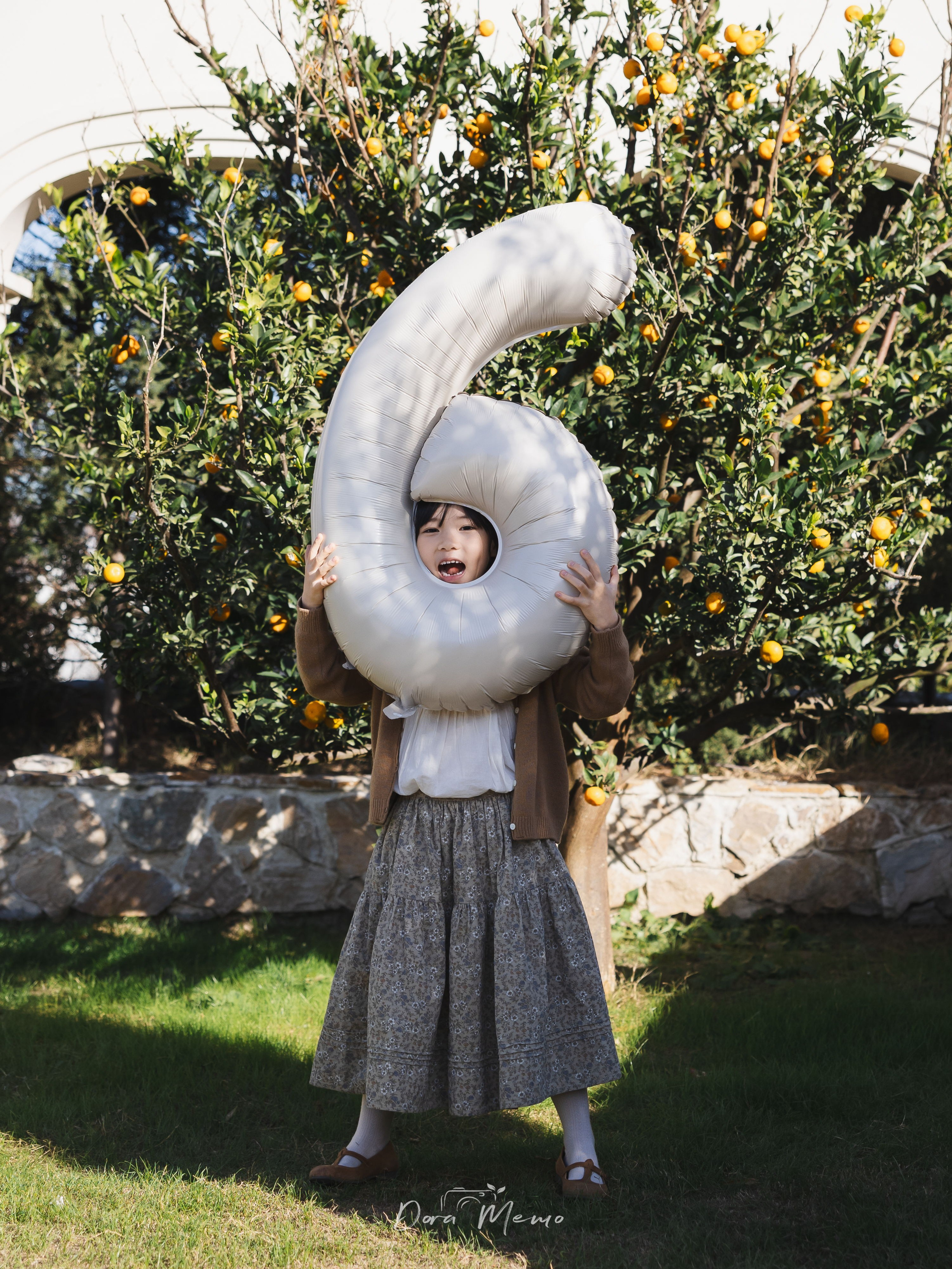Six-year-old girl holding number 6 balloon against blue sky, outdoor birthday documentary photography in Shanghai