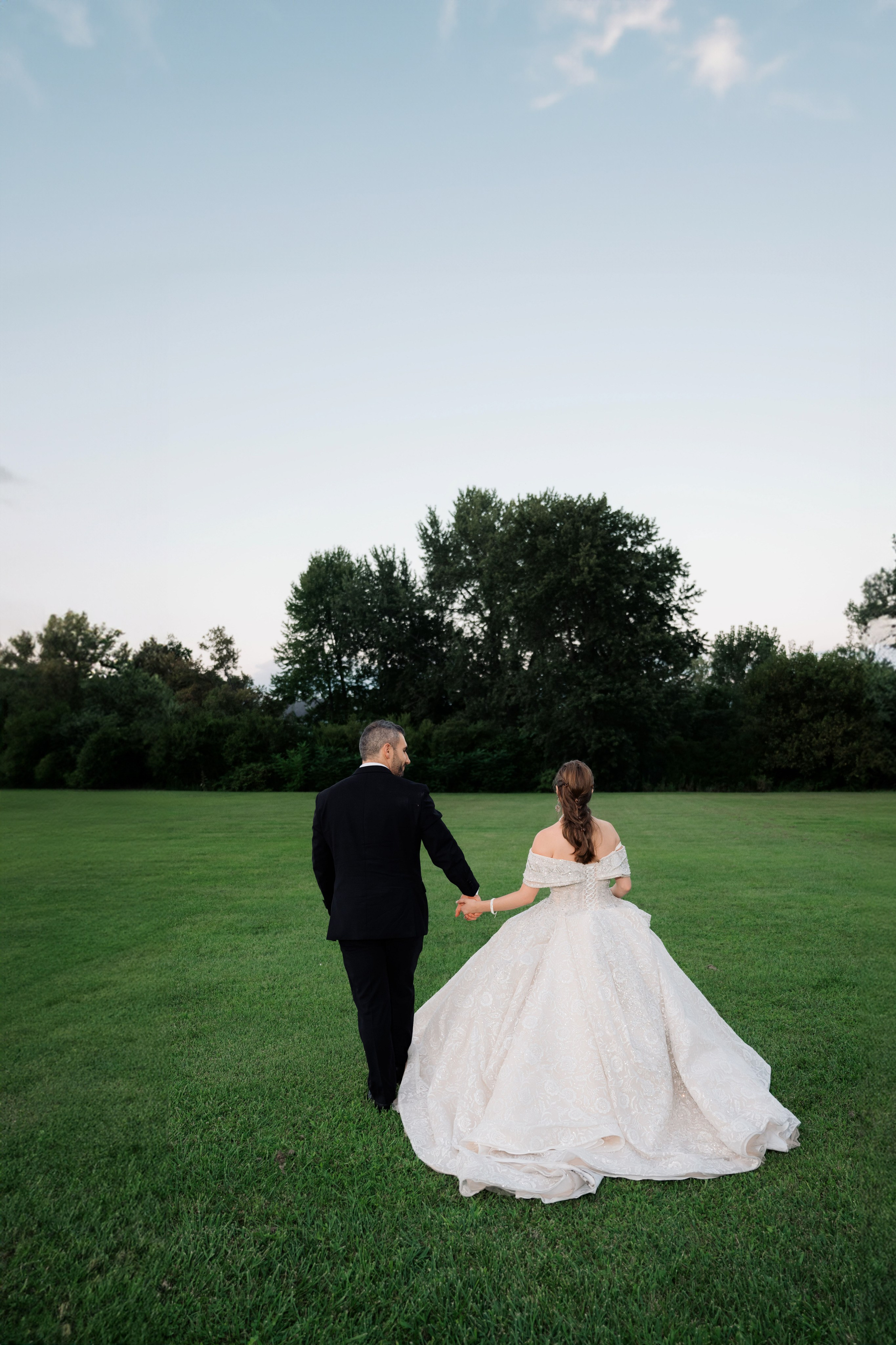 a bride and groom walking through a field
