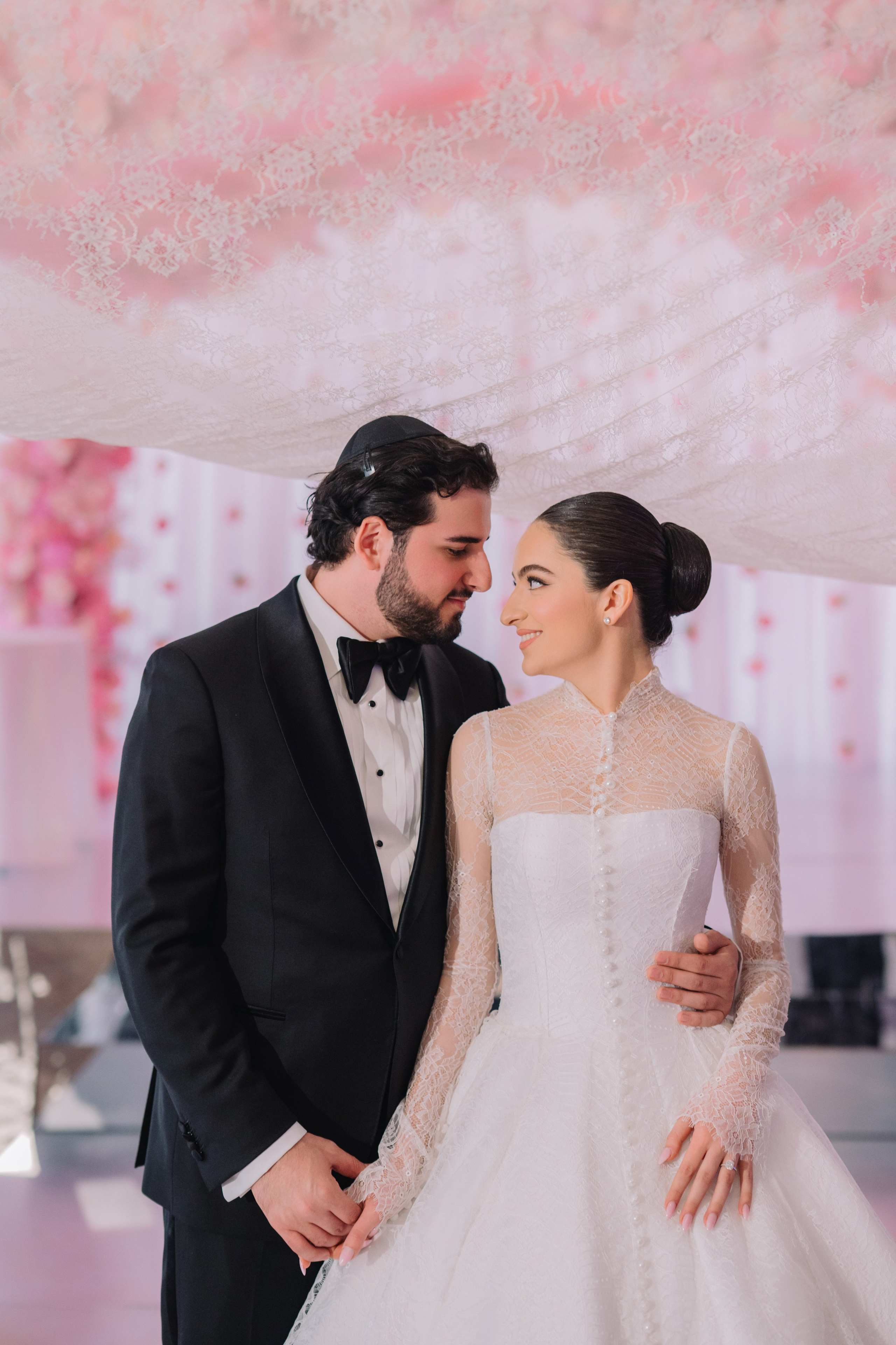 a bride and groom pose under a pink canopy