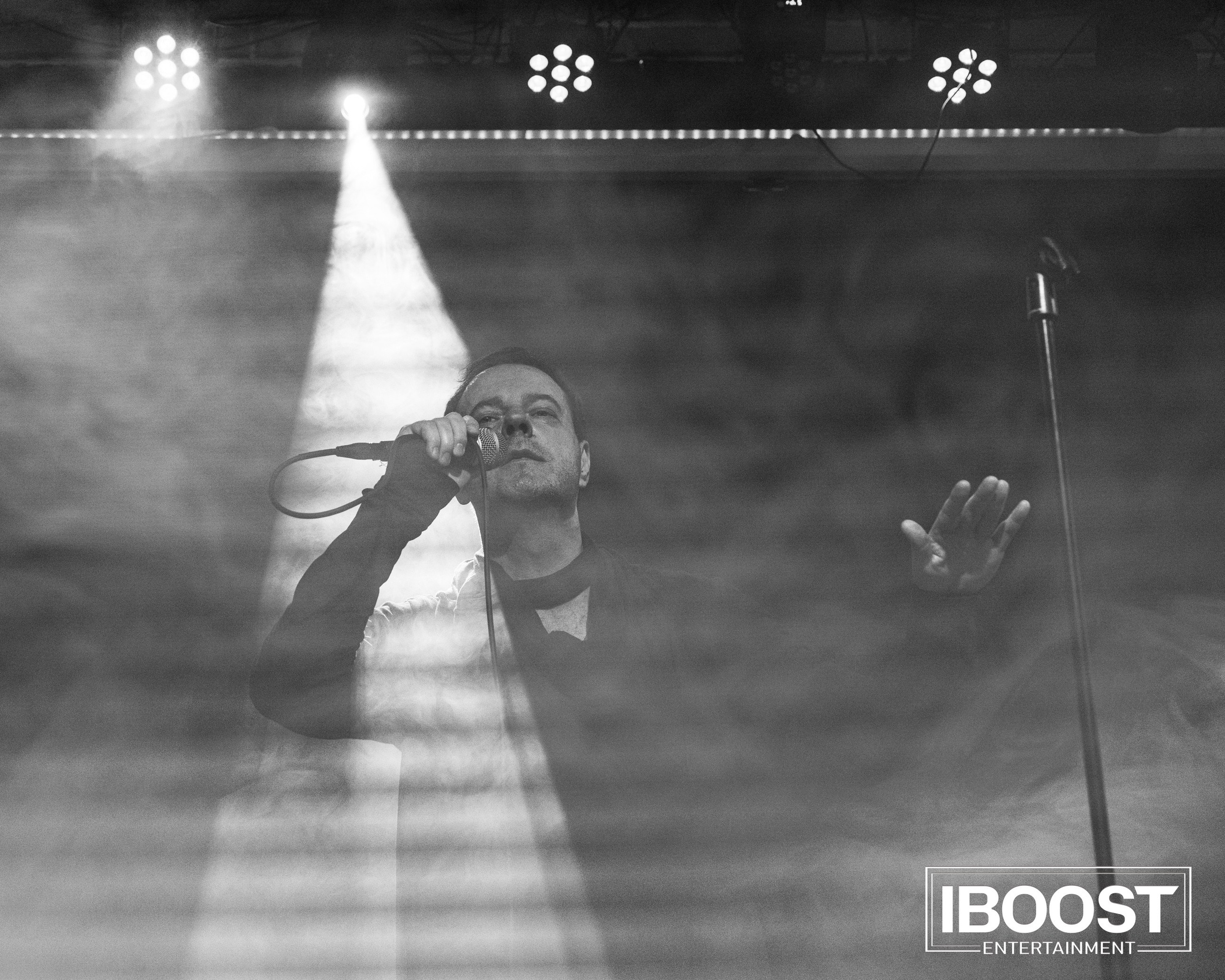 Black-and-white artistic stage photo of the lead vocalist of Animal JazZ under a spotlight and haze.