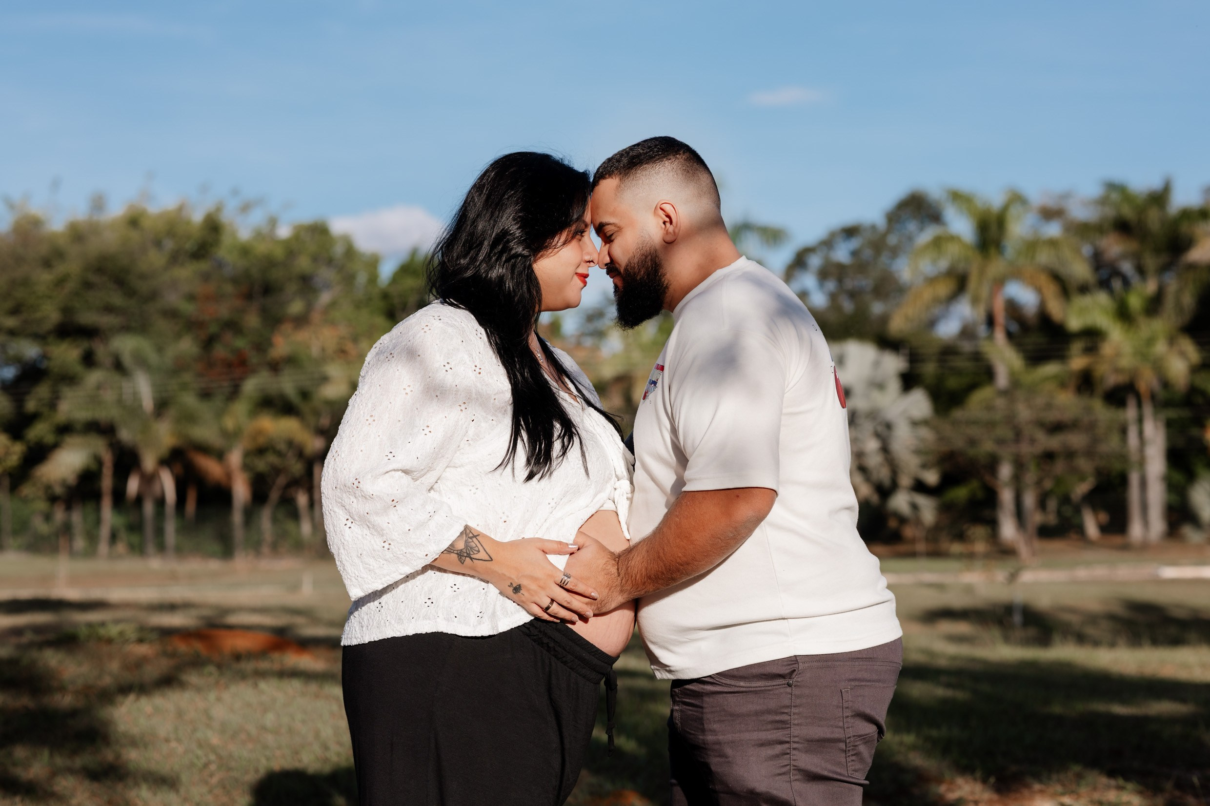 Casal se olha com carinho durante ensaio de maternidade.