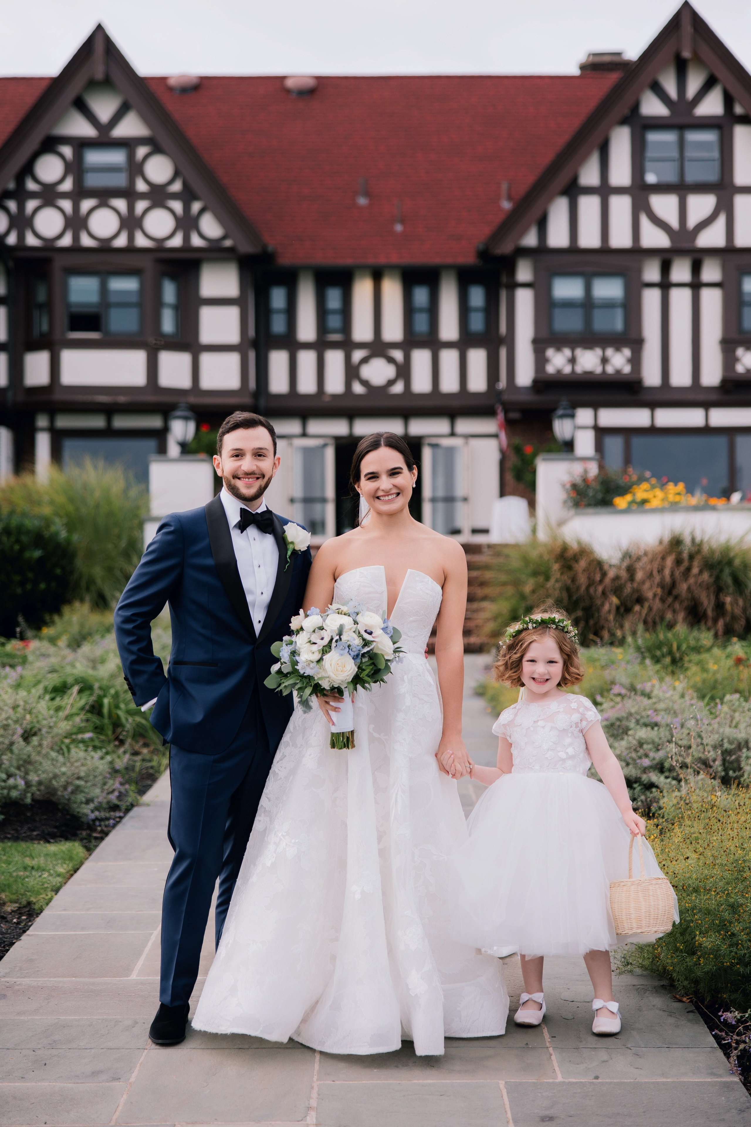 a bride and groom pose for a photo in front of a large house