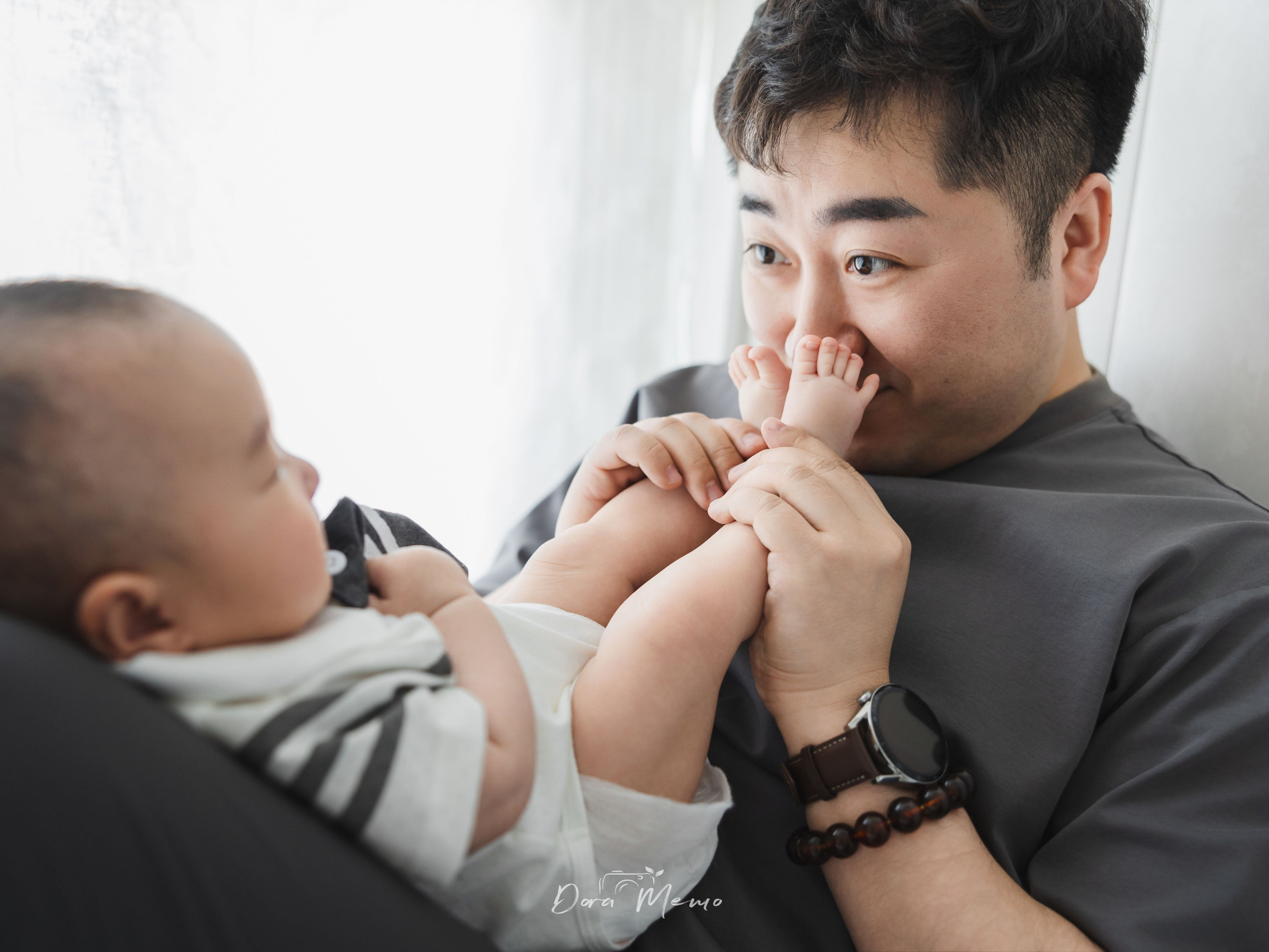 A father smiling and playing with his baby's feet in a relaxed documentary family photograph.