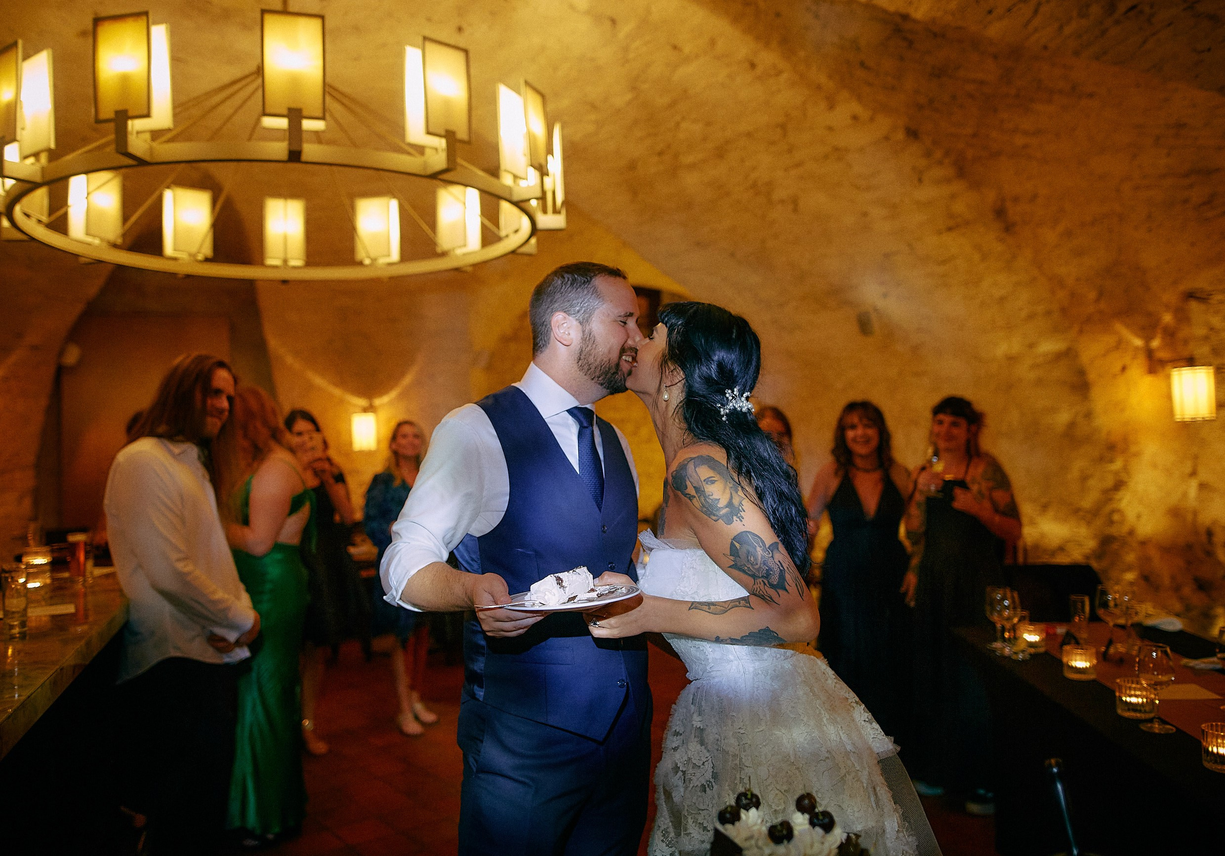 Bride kissing groom while holding wedding cake slice reception.