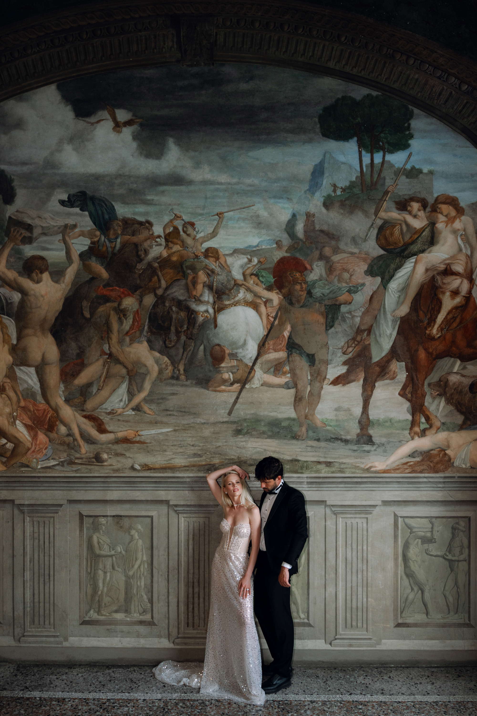 a bride and groom pose in front of a painting