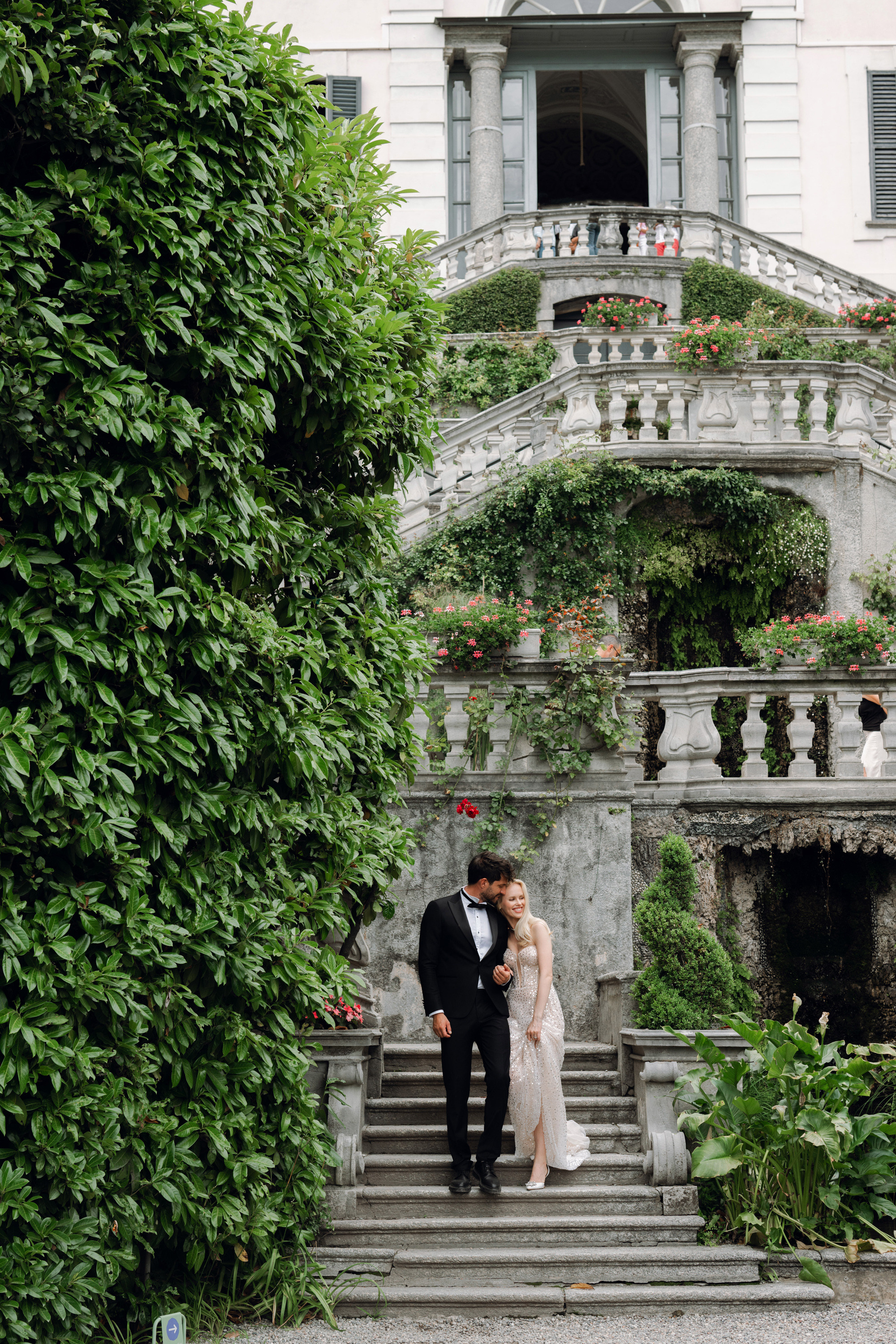 a bride and groom standing on the steps of a mansion