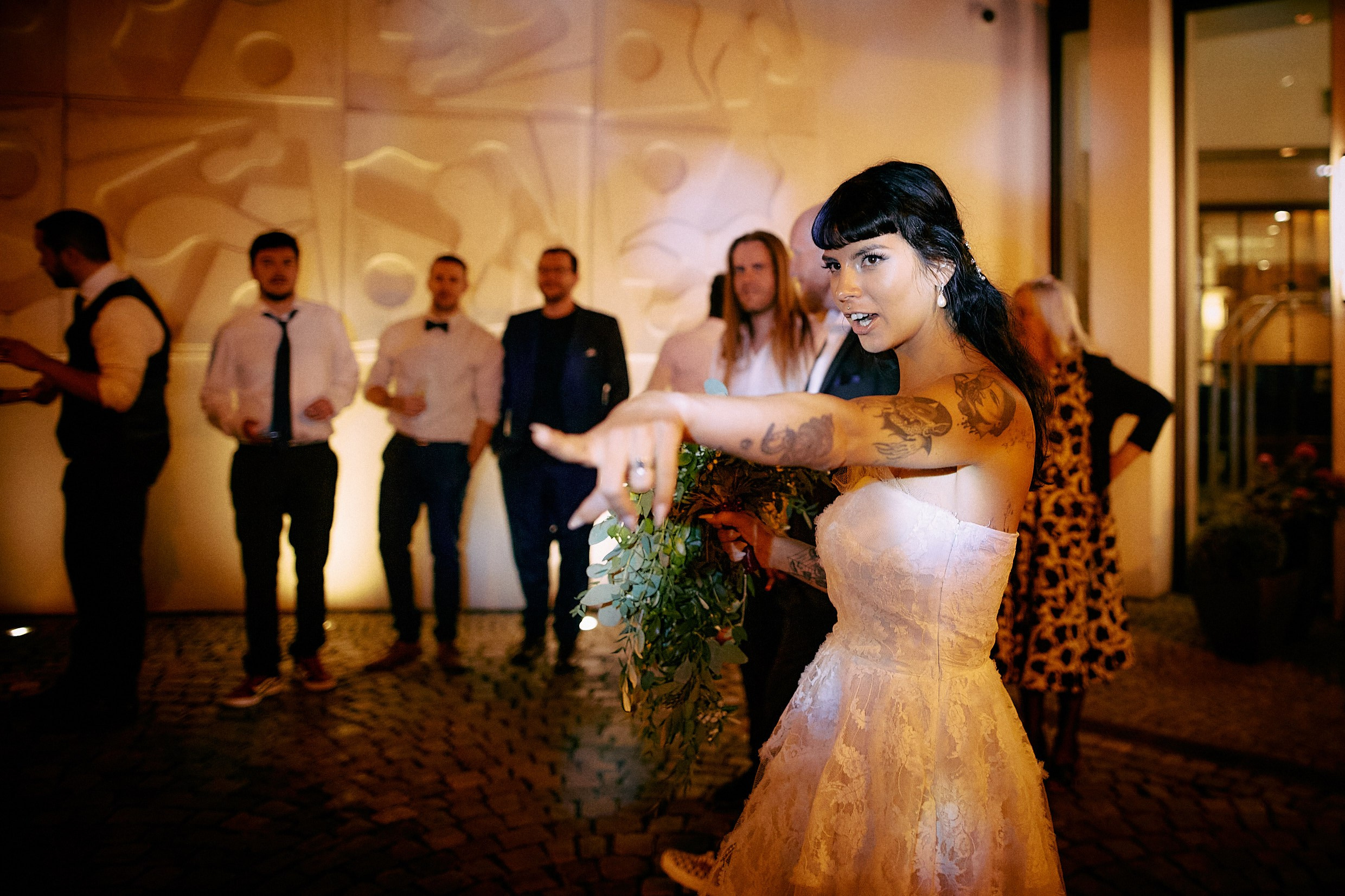 Bride organizing excited female guests for bouquet toss lineup.