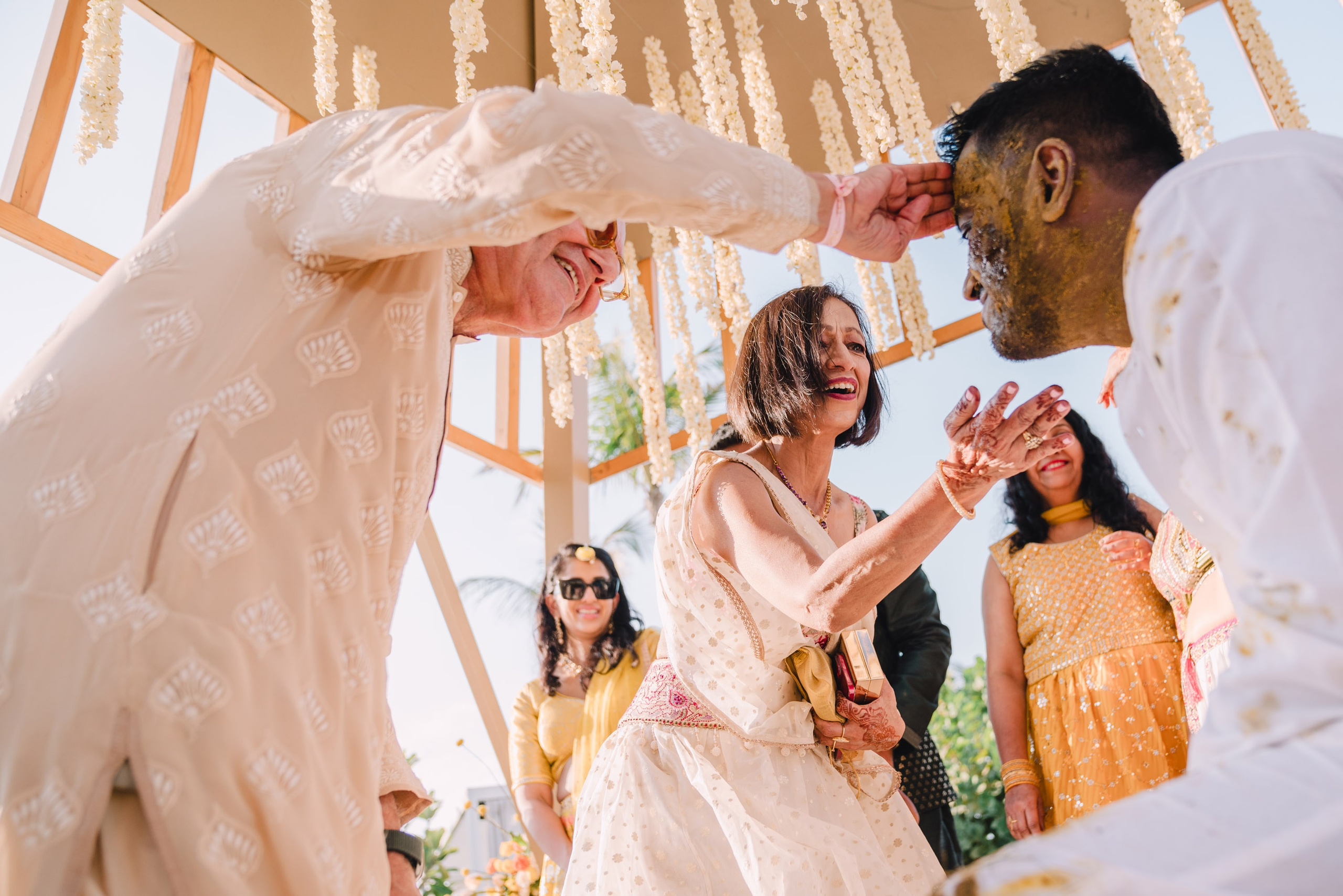 Candid moment of parents touching their son with turmeric and oil during traditional turmeric ceremony