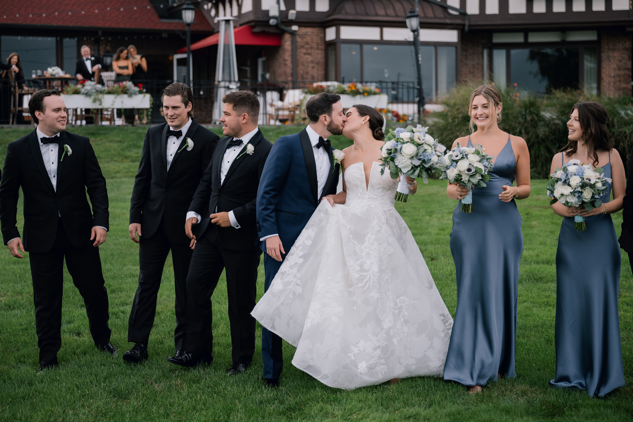a bride and groom kiss as their bridesmaids walk in the grass