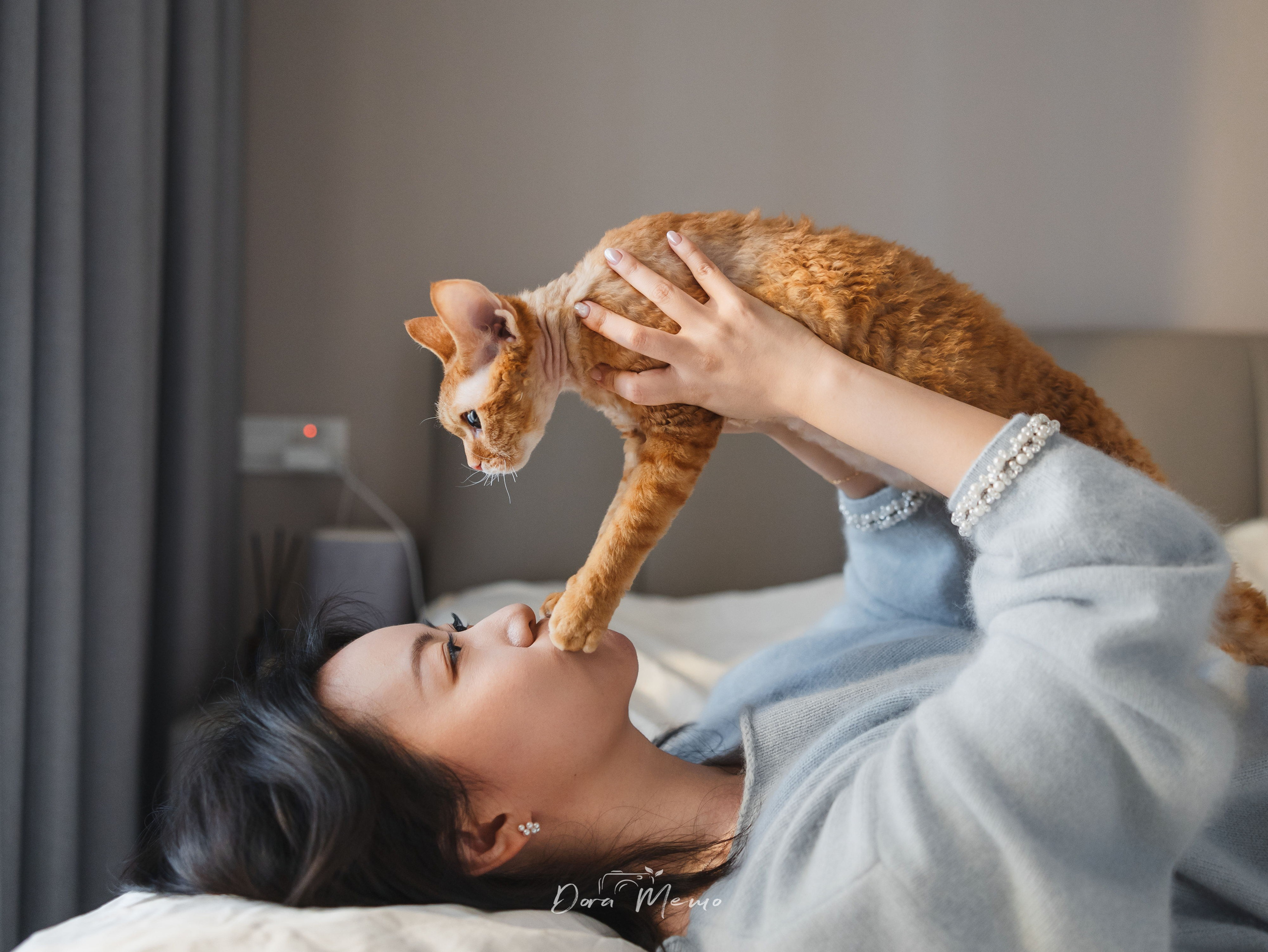 Owner holding her Devon Rex cat on a bed during a warm lifestyle pet photography session