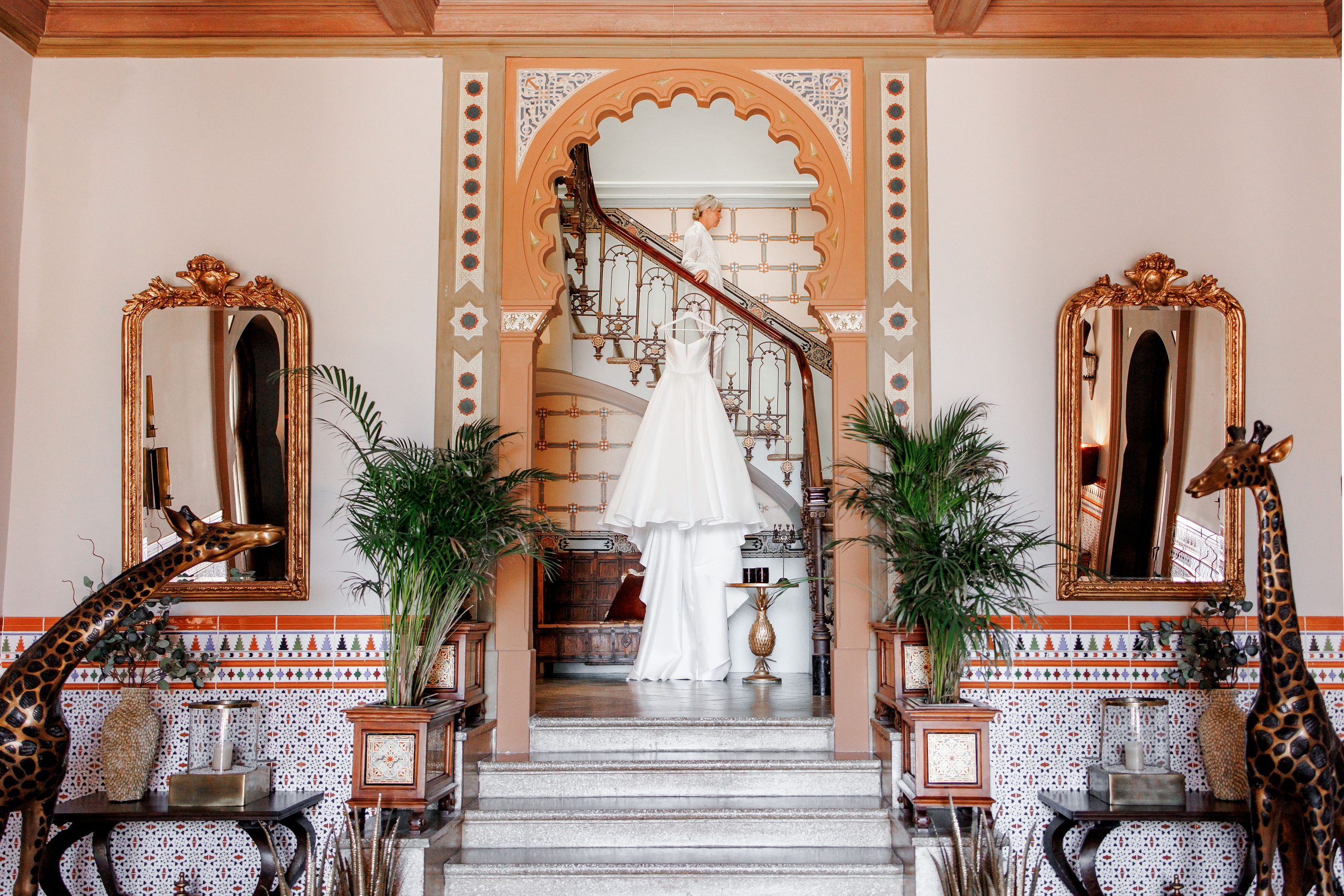 Beautiful shot of a bride walking down the stairs where a stylish wedding dress hangs.