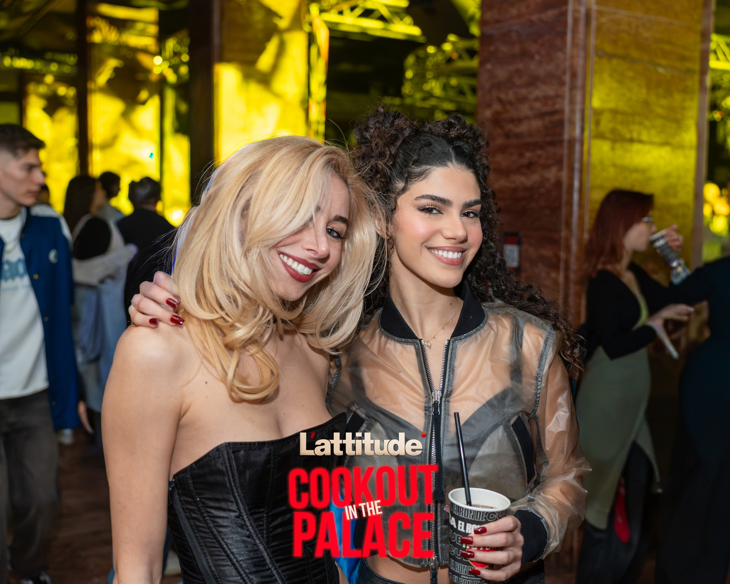 Two women smiling at an indoor social event, one holding a drink cup.