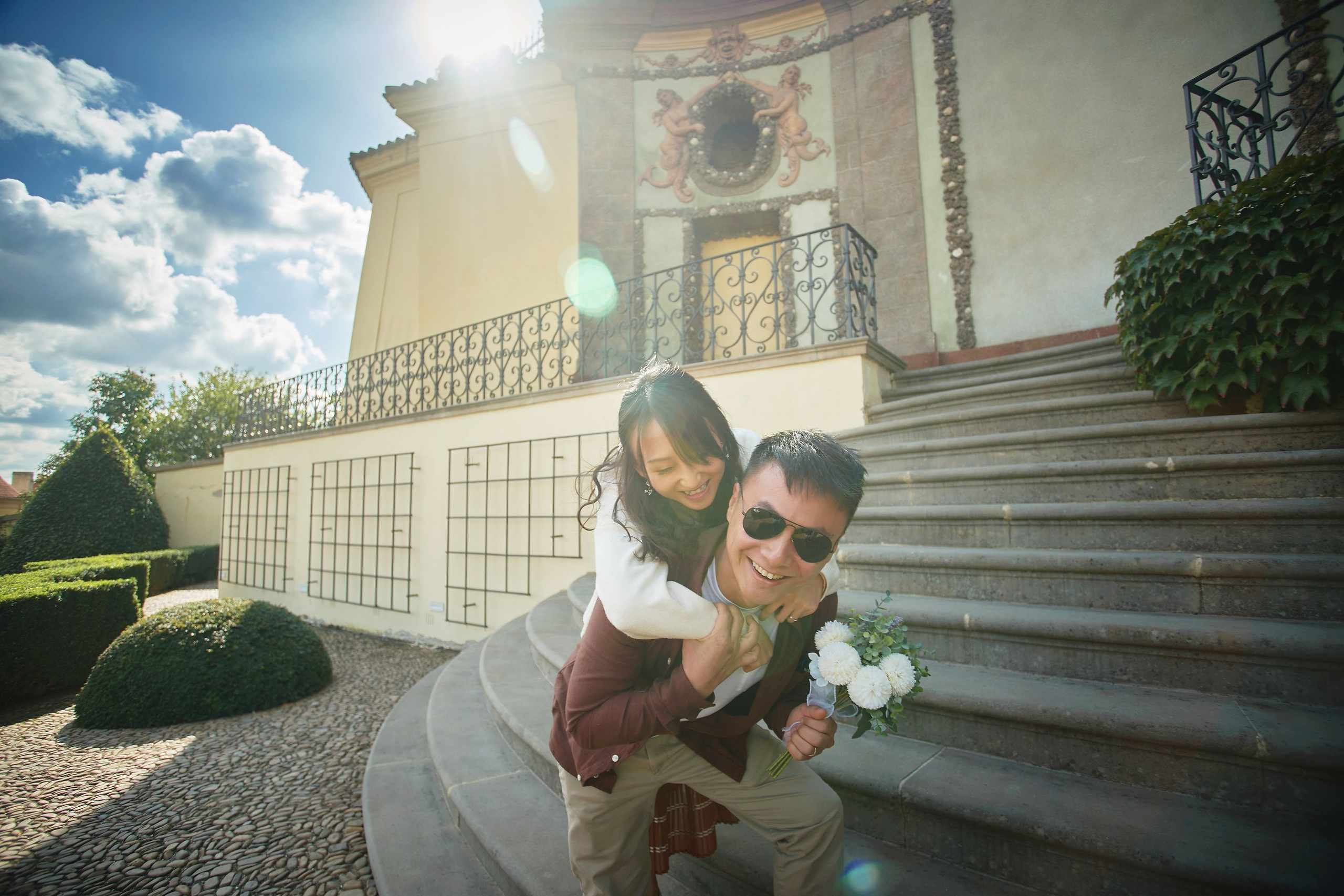 Conan is carrying Eva on his back while holding a bouquet in Vrtba Garden.