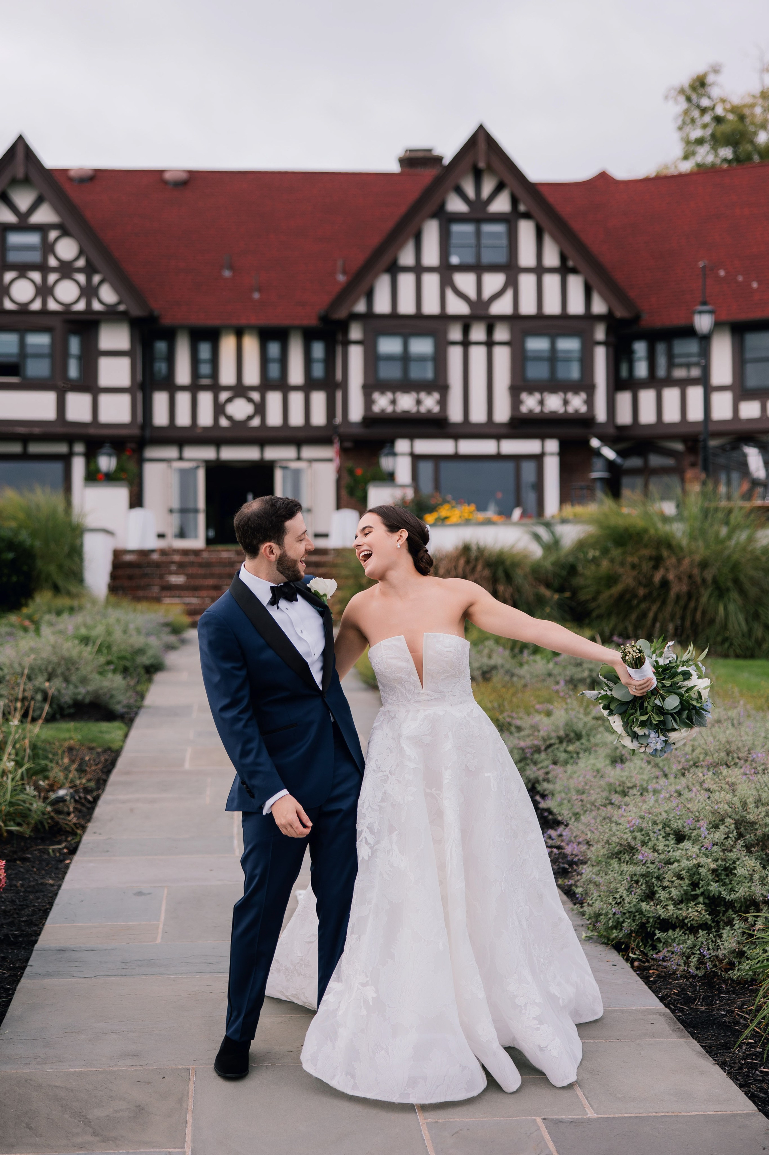 a bride and groom pose for a photo in front of a large house