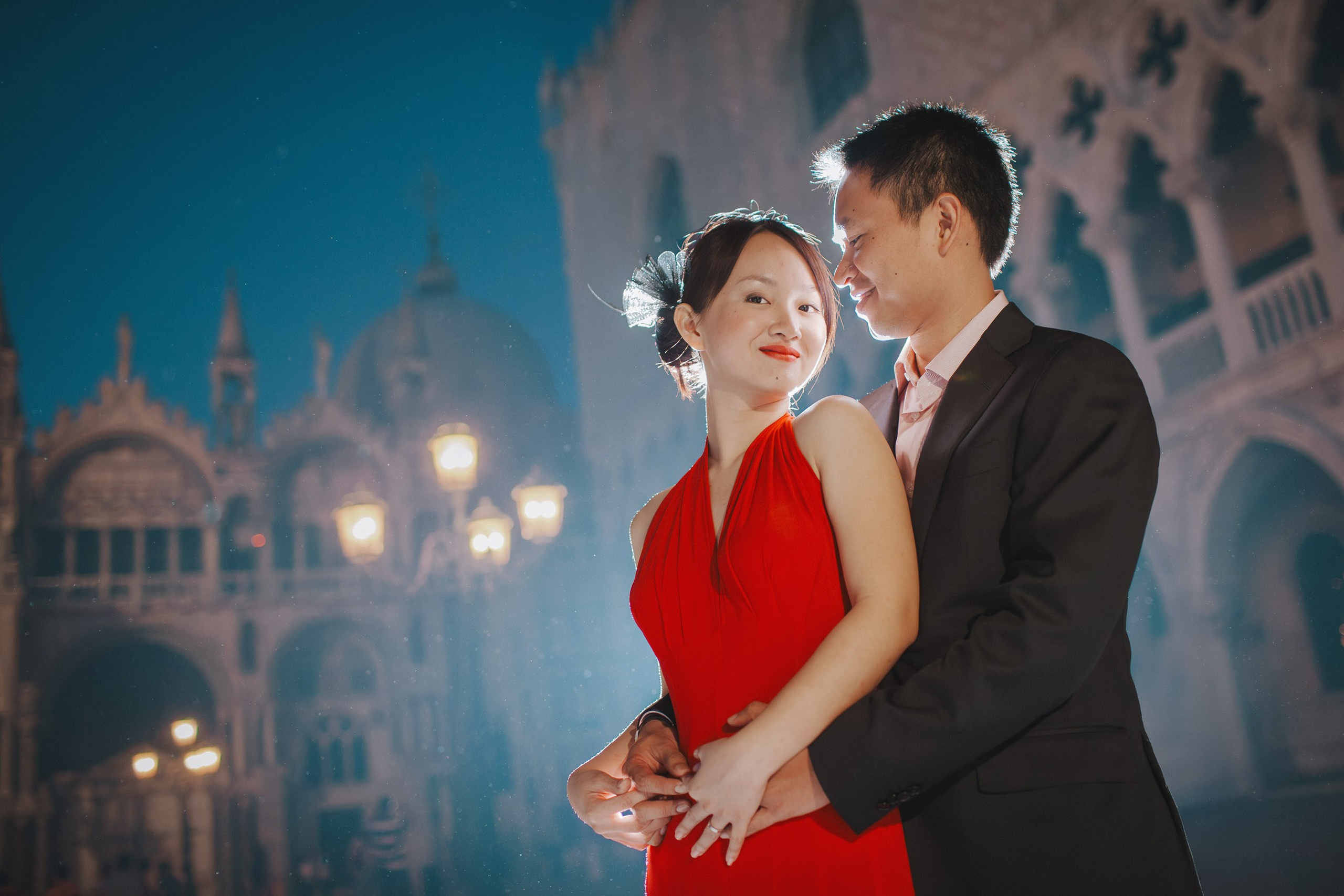 A couple embrace near the gas lamps in front of the Doge's Palace during their night time portrait session in the historic San Marco square in Venice.