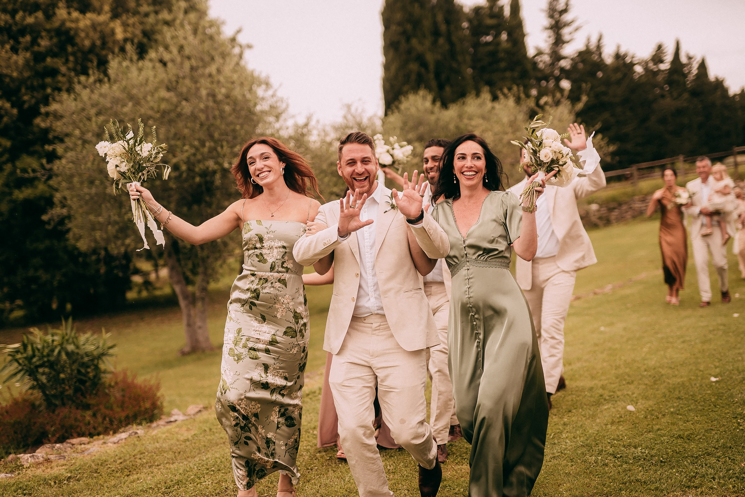 Wedding party members energetically joining the bride and groom, waving their hands and bouquets in celebration.