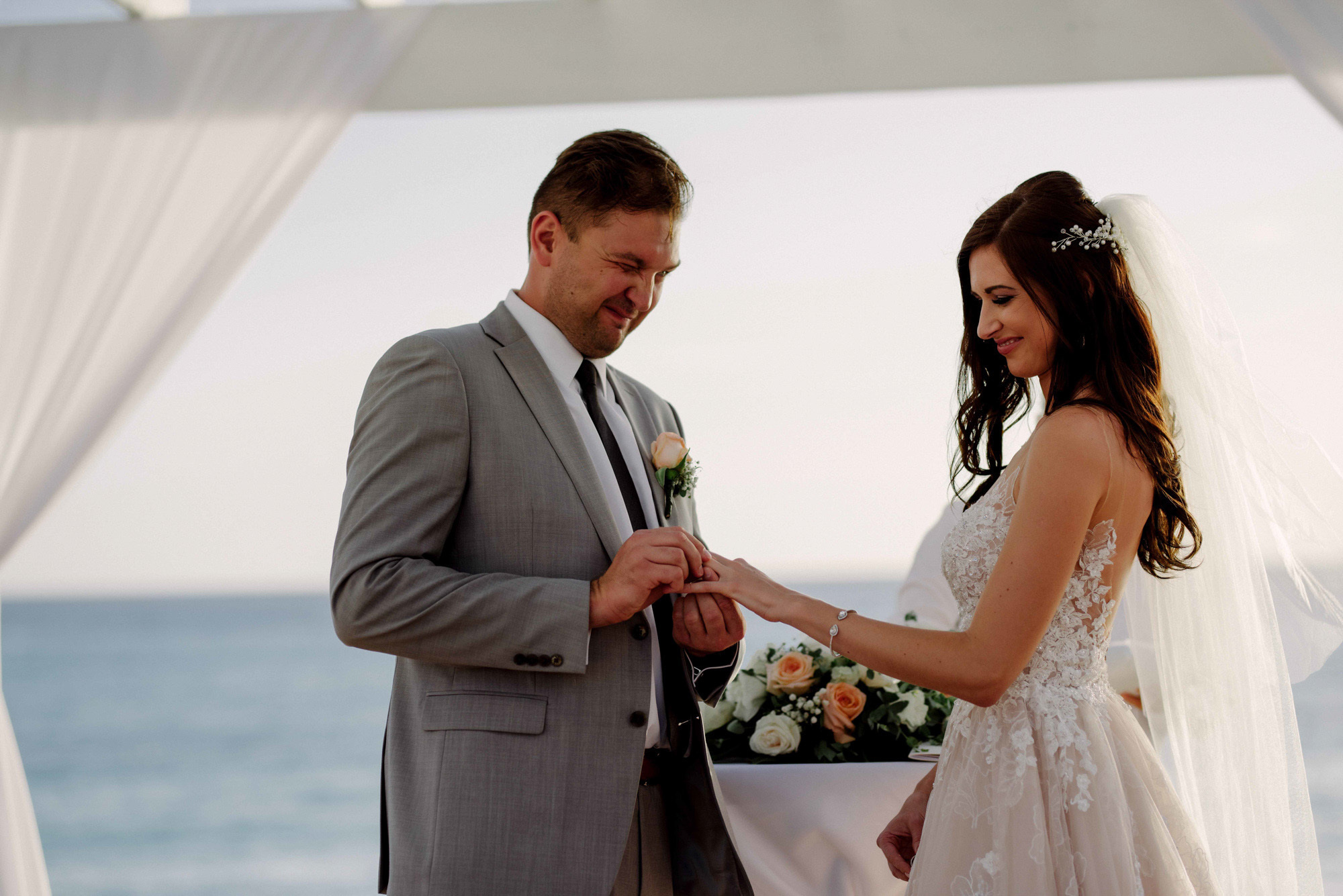 The groom at the altar puts a ring on the bride's finger against the background of the sea.