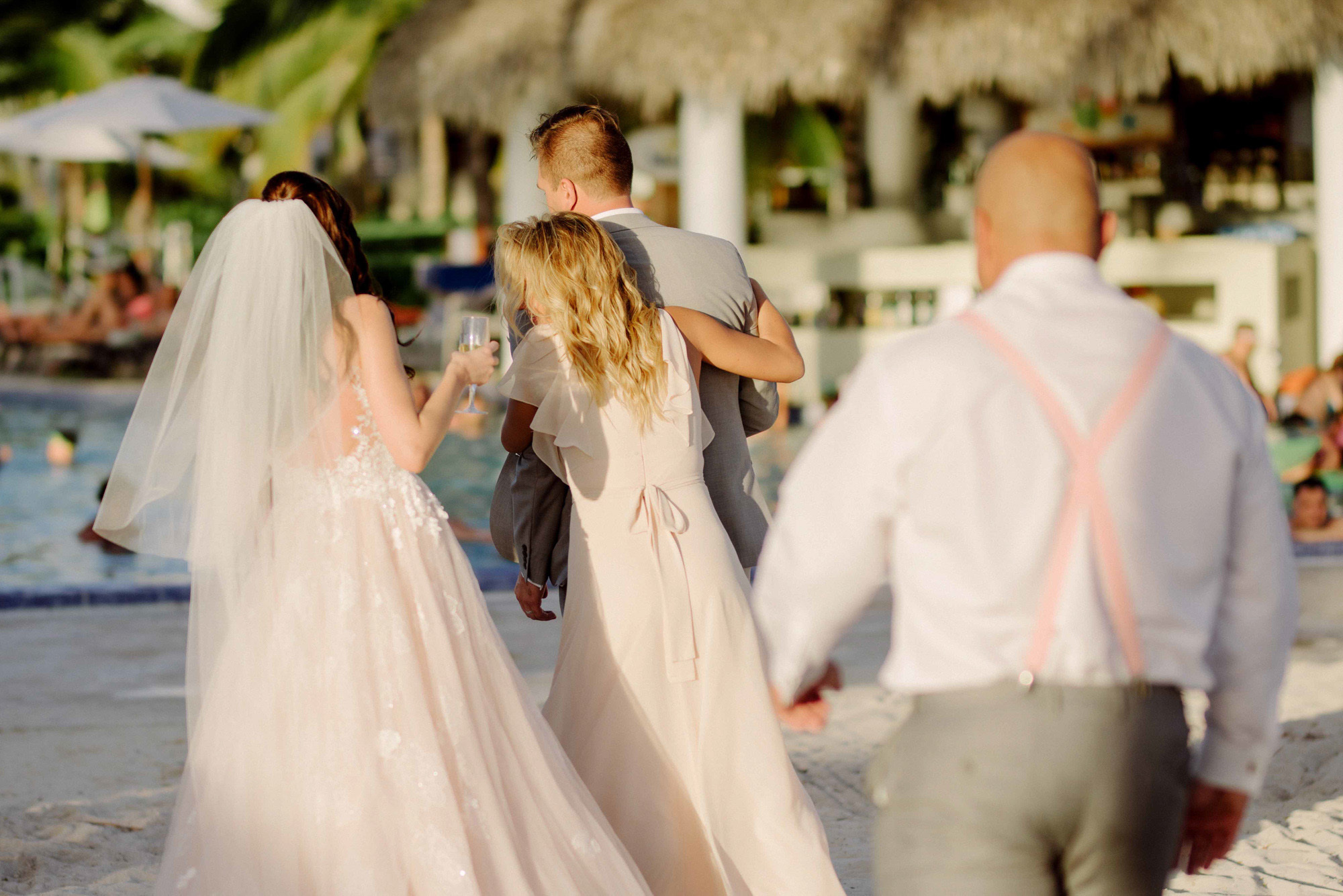 Bride, groom, mom and dad walk on the beach with the background of the beach bay.