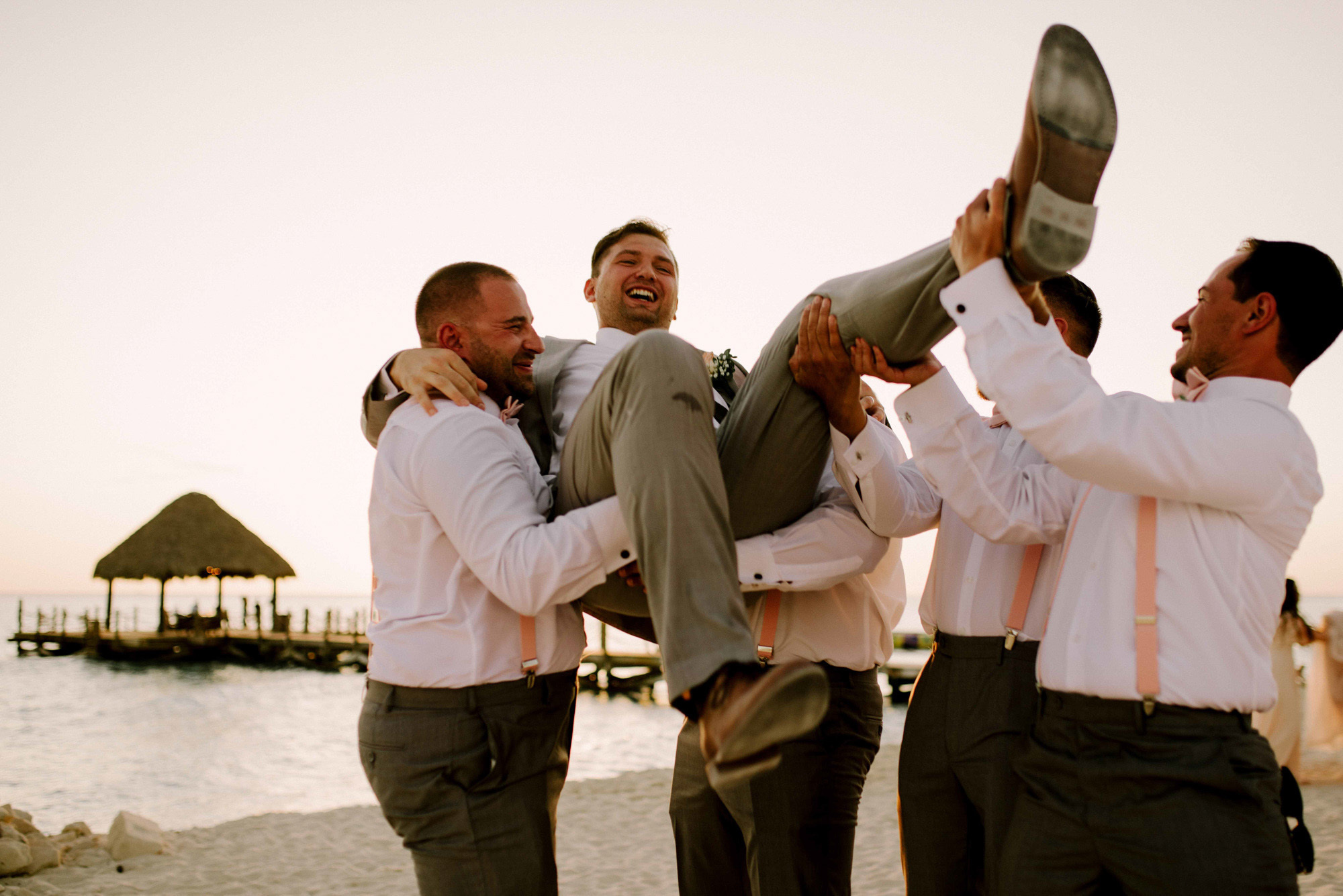 Friends toss the groom in their arms against the background of the sea beach and beach houses.