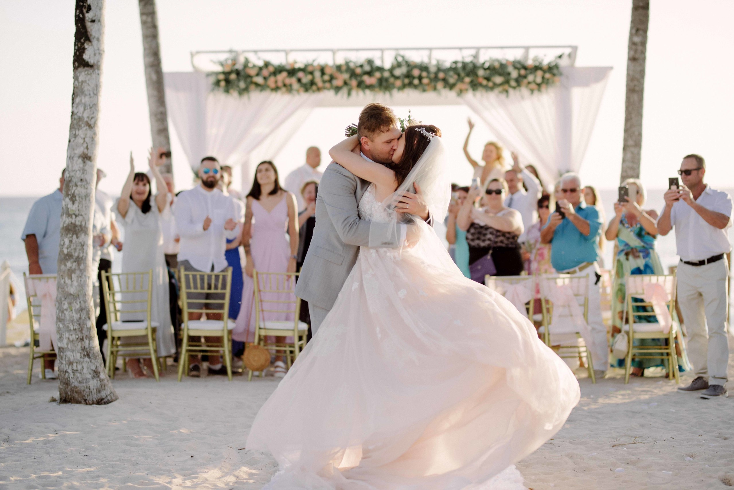 Bride and groom embrace in front of wedding guests.