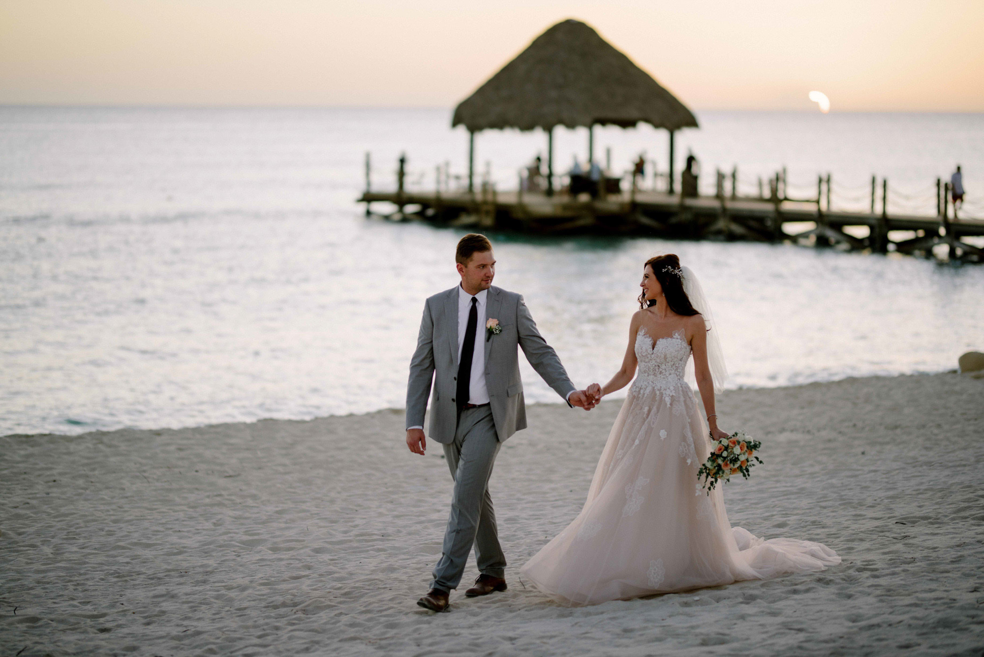 The bride and groom walk along the evening beach.