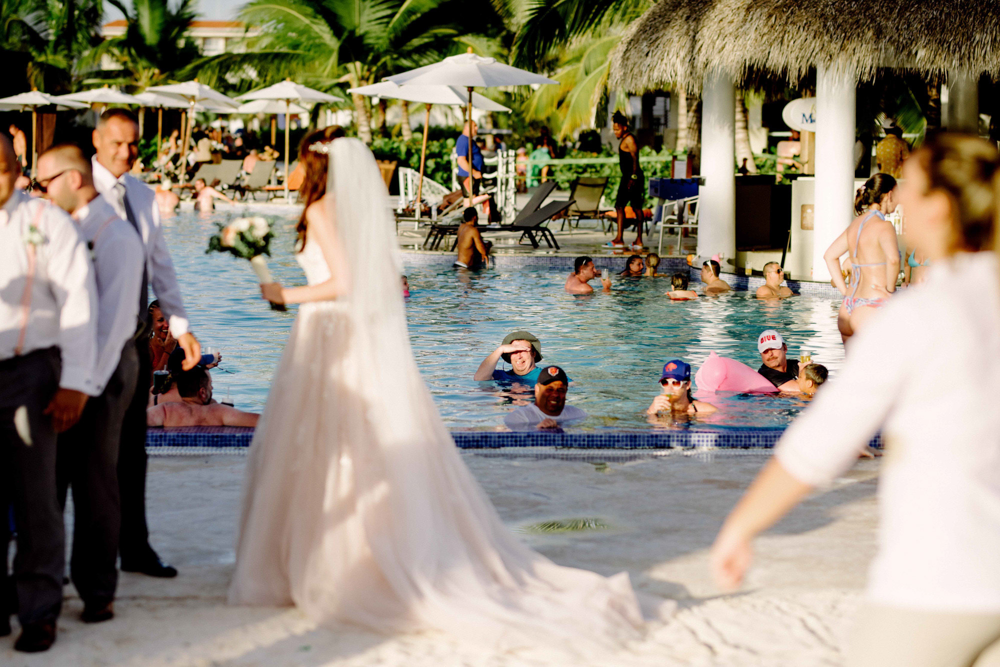 The bride stands on the beach among bathing vacationers surrounded by guests.
