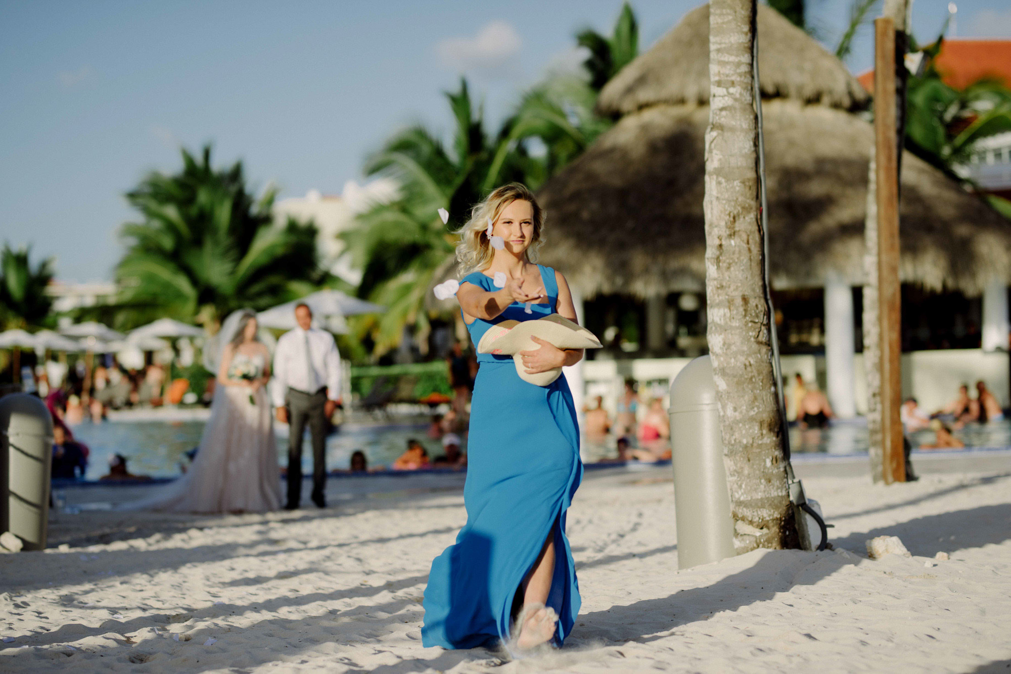 Blonde girl stands on the background of newlyweds and festive tables on the background of the beach with palm trees and beach houses.