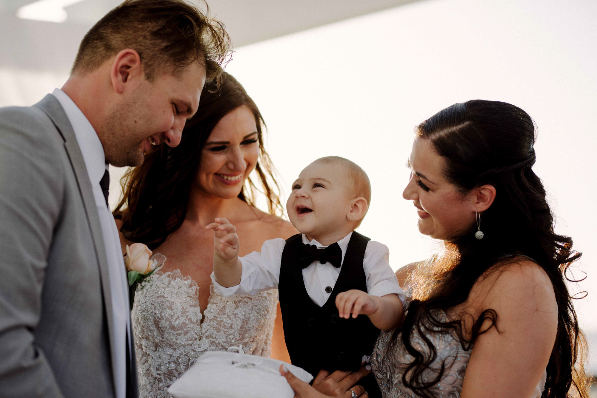 The bride and groom. A baby in the arms of a woman holds out a pen to the groom.