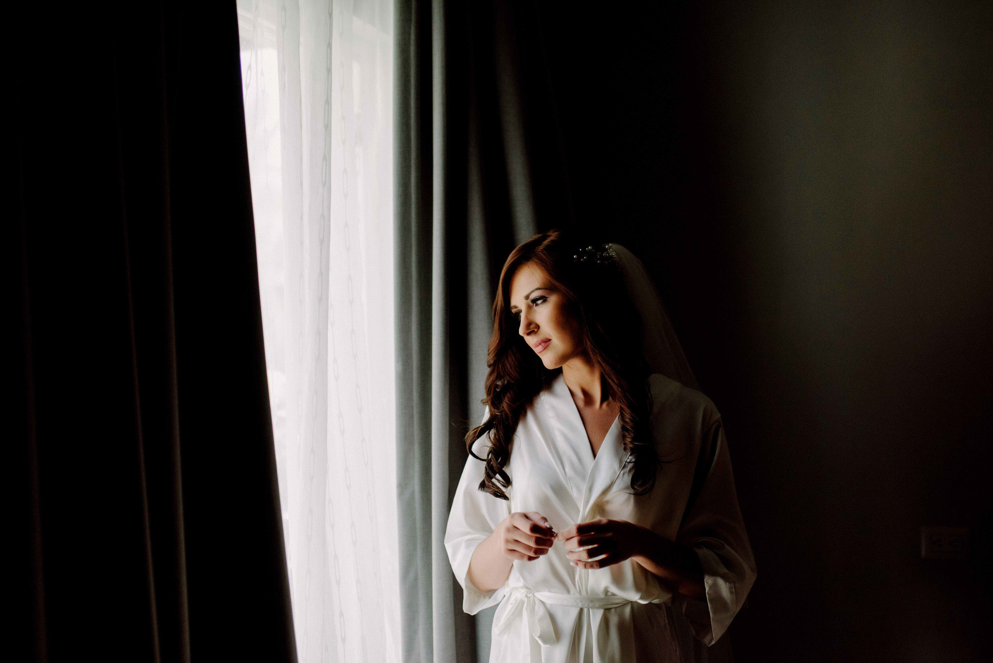 A dark-haired girl in a white lab coat looks out the window.