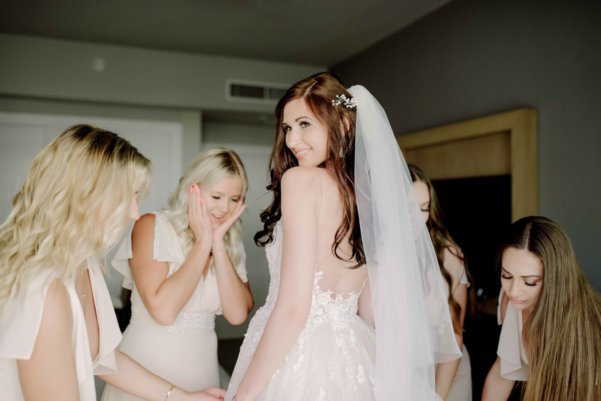 The bride in a veil and a wedding dress with an open back surrounded by admiring friends.
