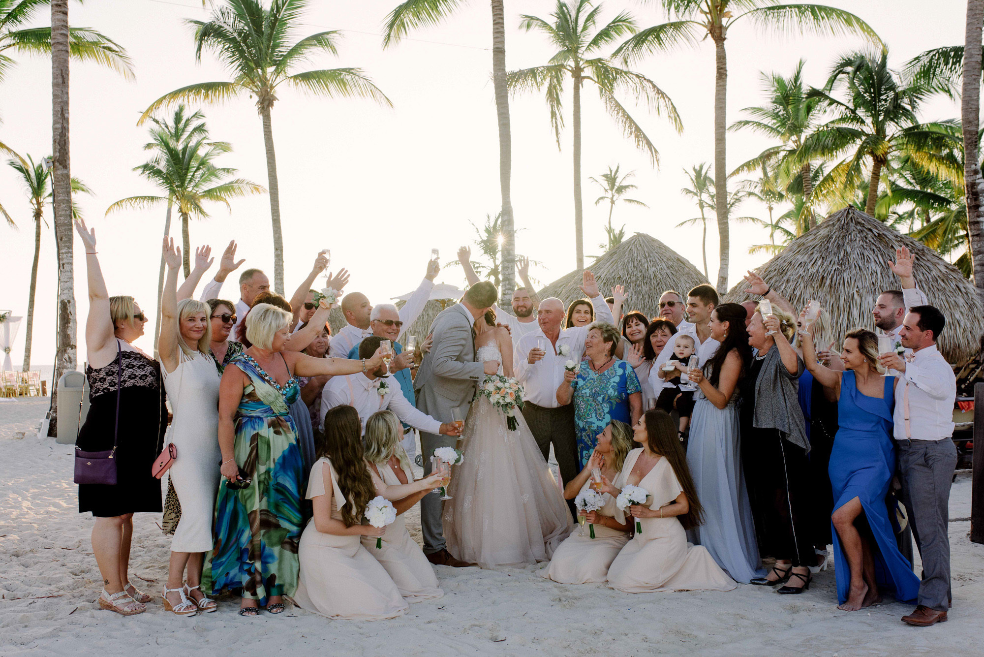 All the guests and the bride and groom gathered for a joint photo on the background of the sea beach with palm trees.