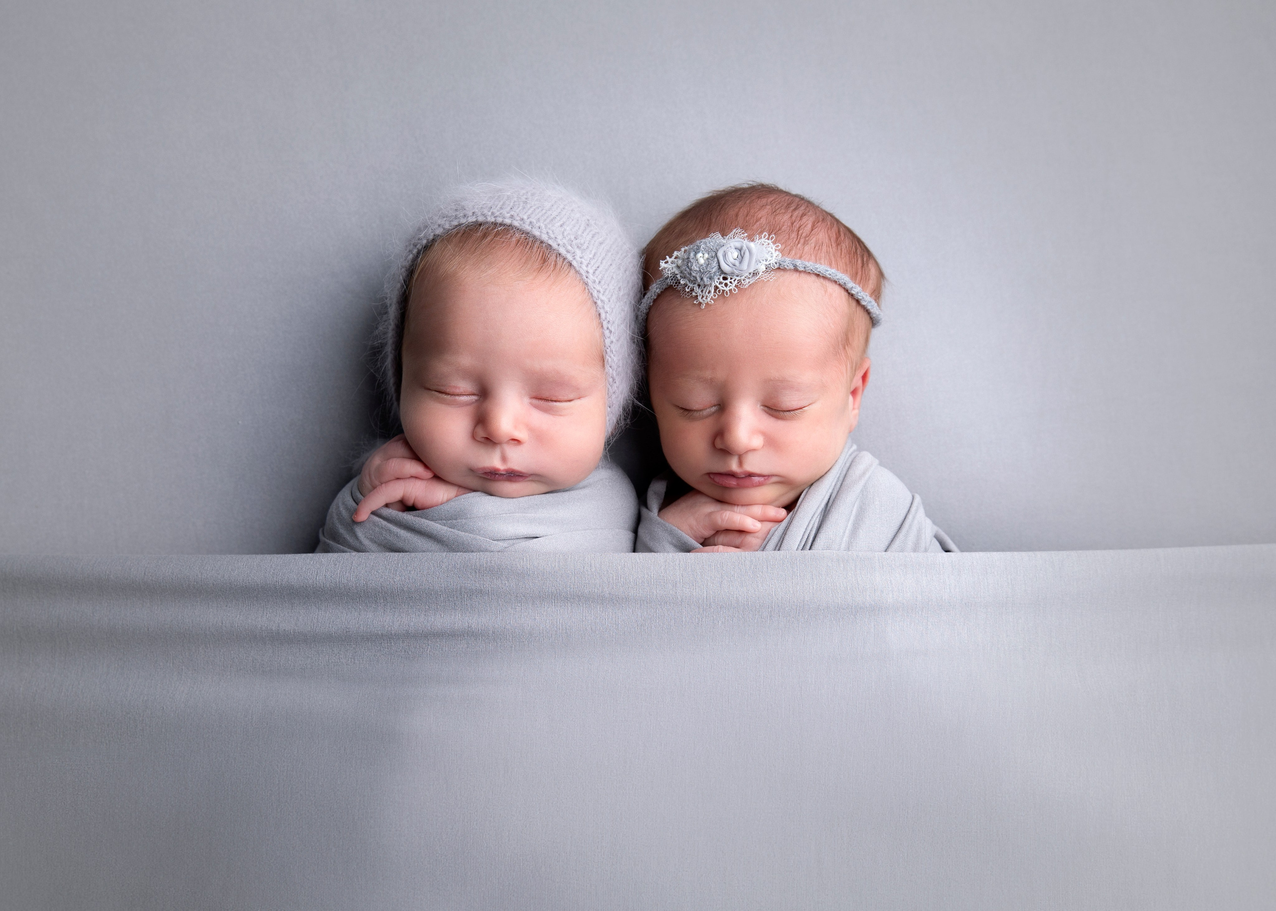 Två nyfödda tvillingar som ligger tillsammans i en mjuk filt. Bilden fångar deras söta och harmoniska utseende, perfekt för att illustrera tvillingfotografi och nyfödda bilder."