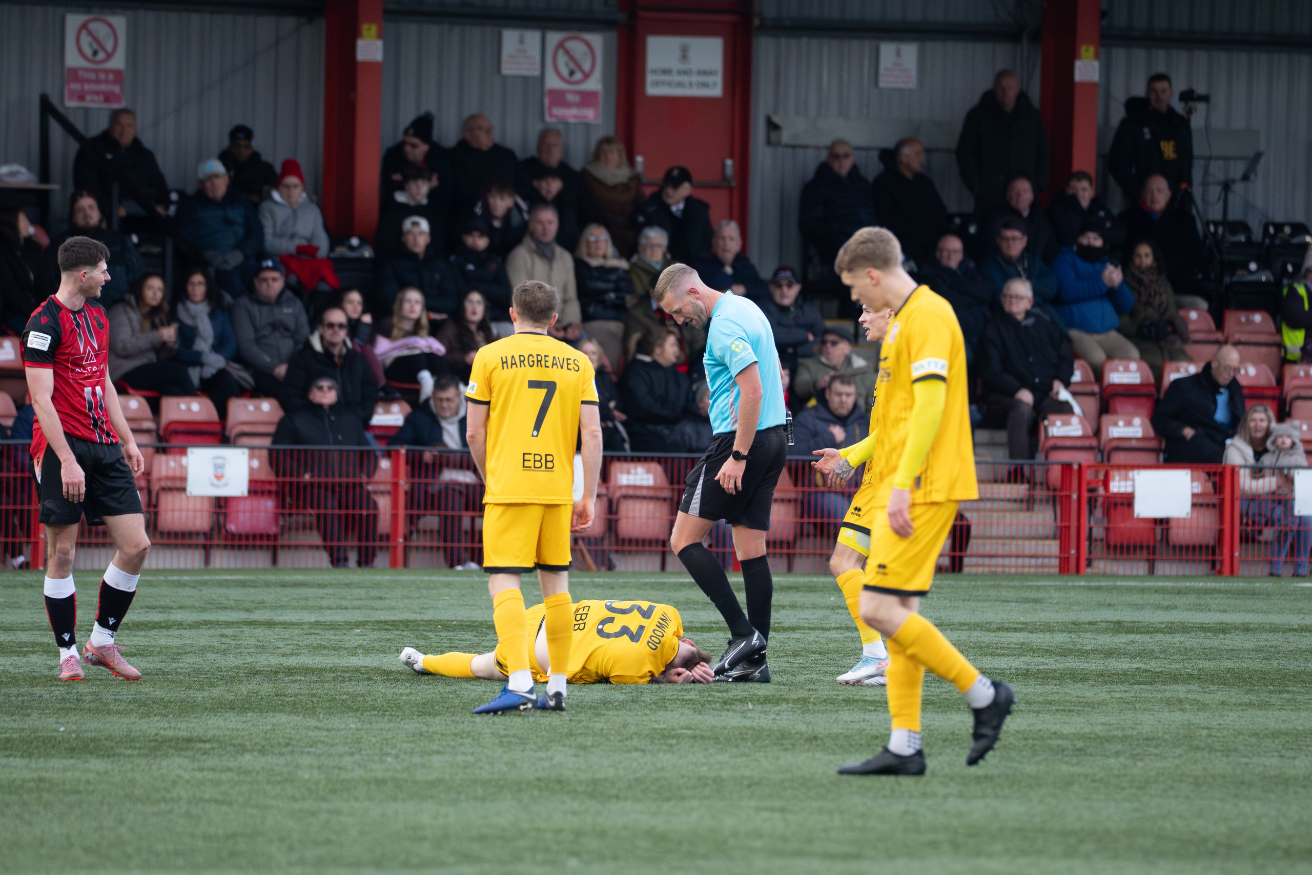 Tamworth, England — February 14, 2026: Aldershot Town’s Sam Inwood receives treatment after going down injured as referee Jamie O’Connor looks on during the Enterprise National League match between Tamworth and Aldershot Town at The Lamb Ground. Photo: Jay Soundo