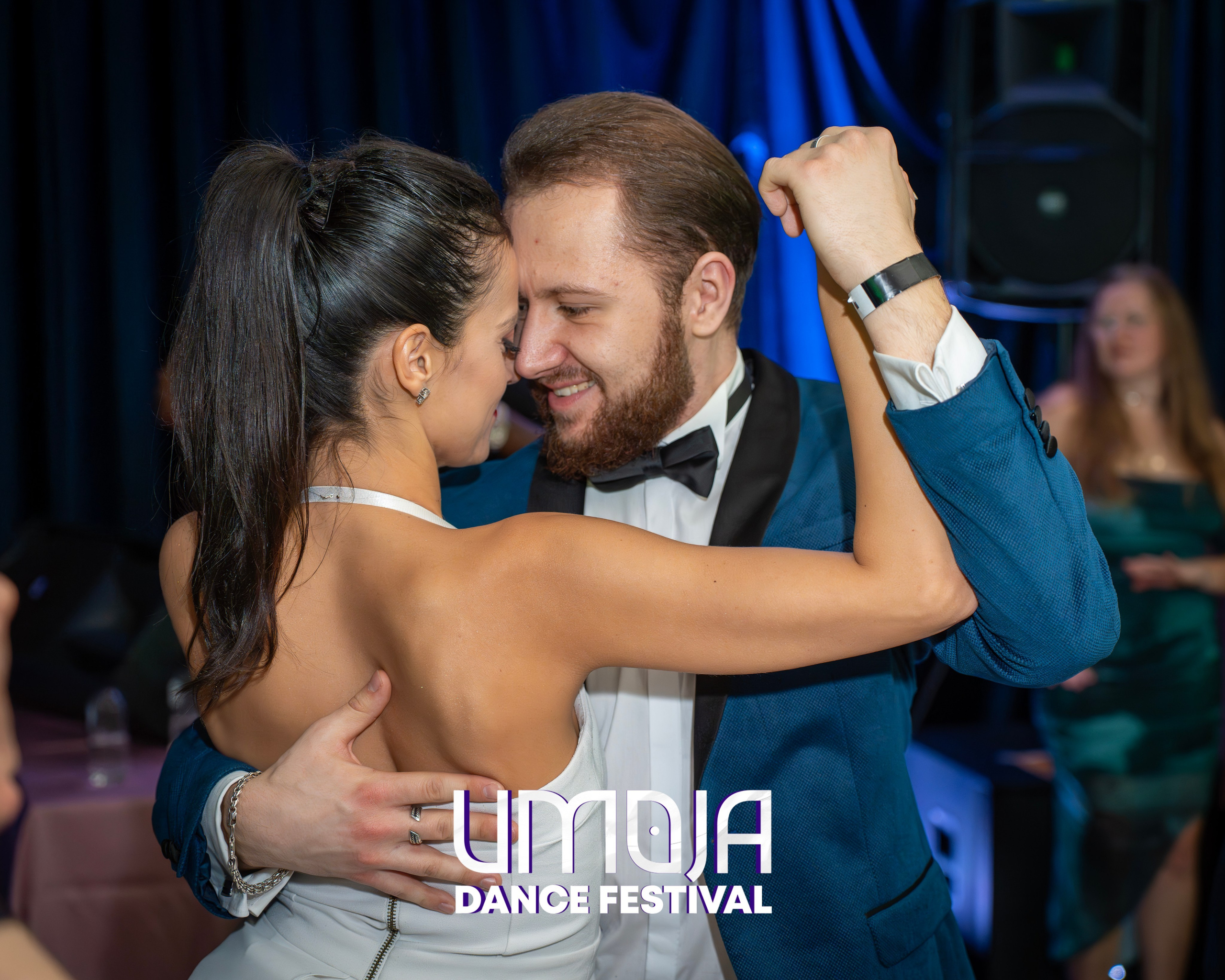 Couple dancing closely at an indoor event with blue lighting in the background.