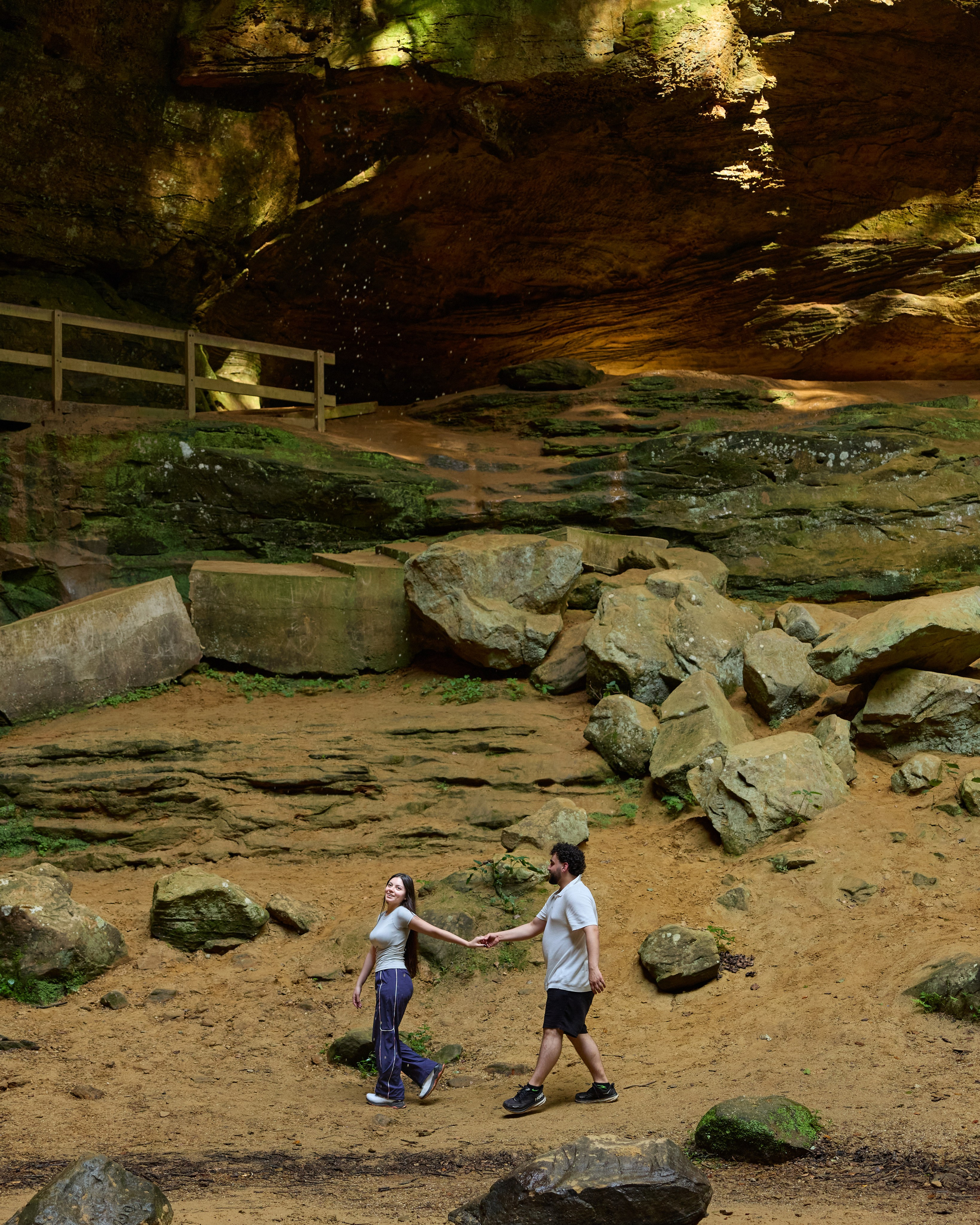 Newly engaged couple walking hand in hand through a rocky gorge in Hocking Hills, Ohio
