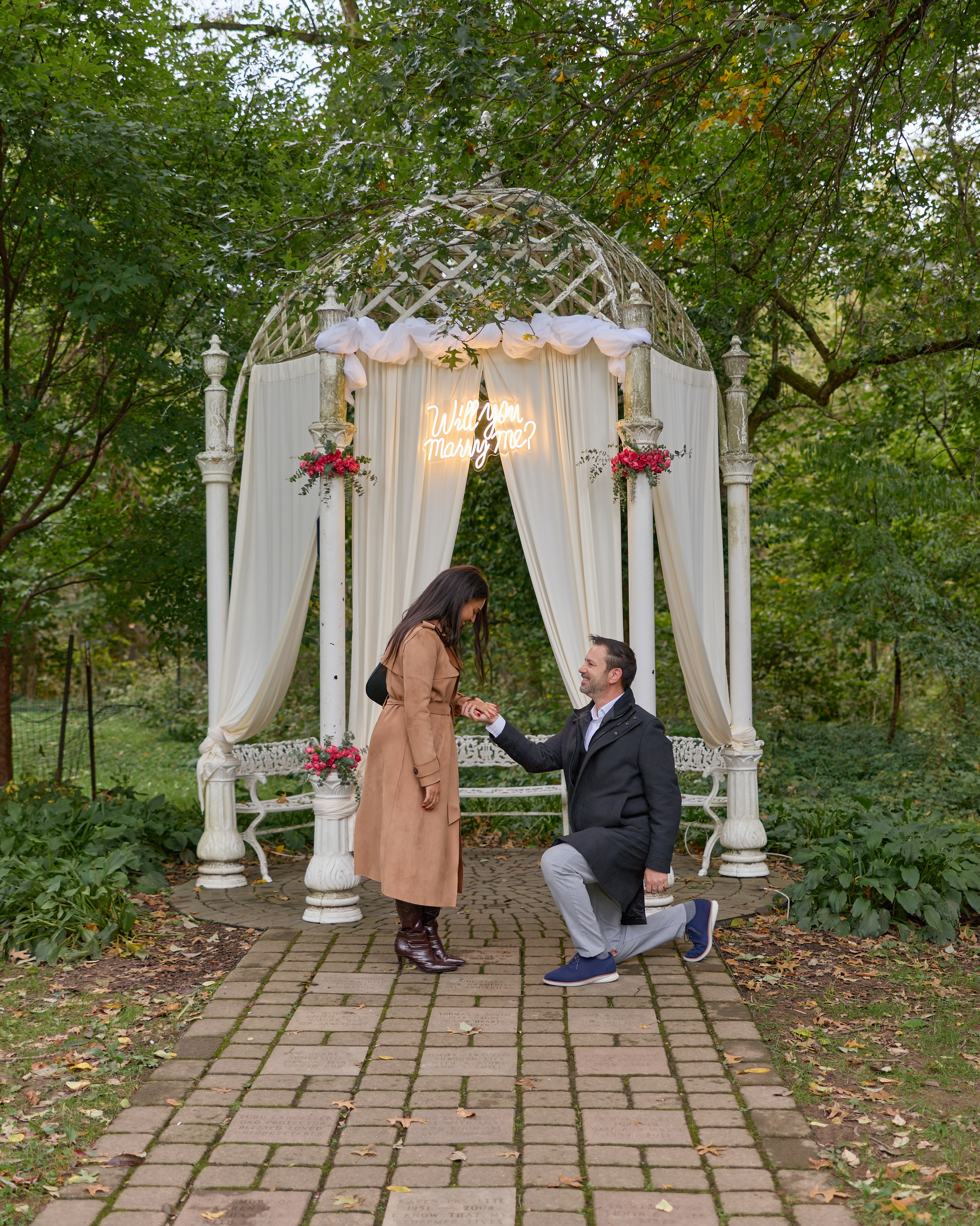 Kneeling proposal under a flower-decorated white gazebo at the Columbus Park of Roses
