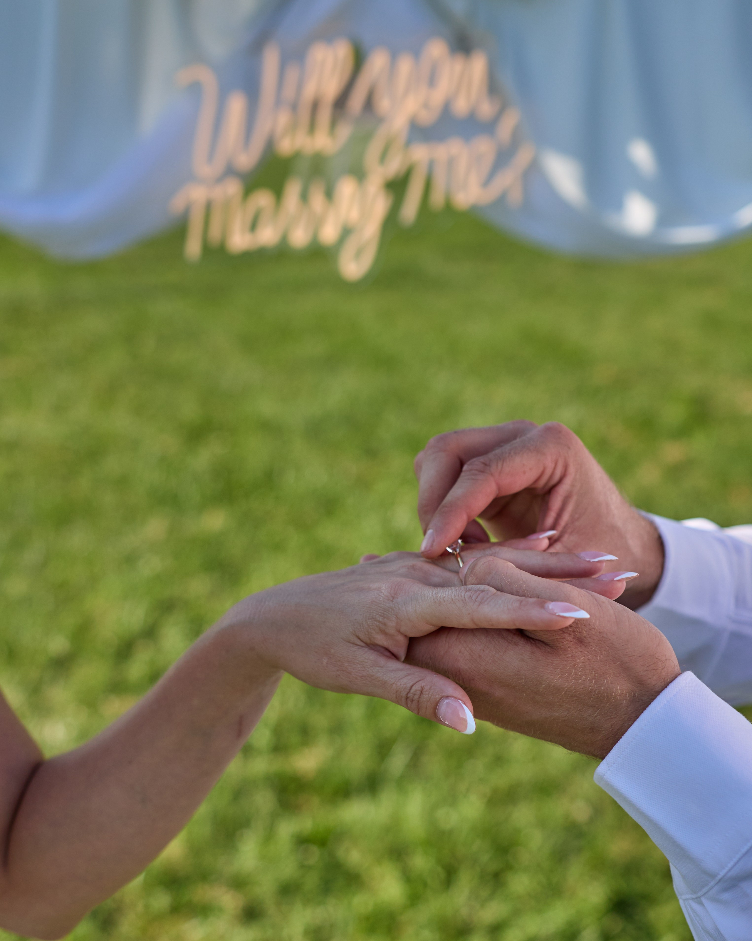 Close-up of the ring exchange with the "Will you marry me?" sign behind at Alum Creek, Ohio